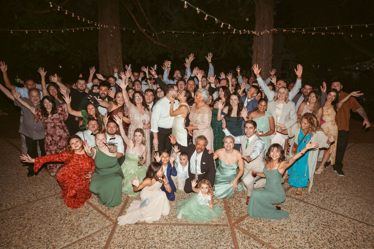 Wedding guests dancing and celebrating at an outdoor evening reception under string lights.