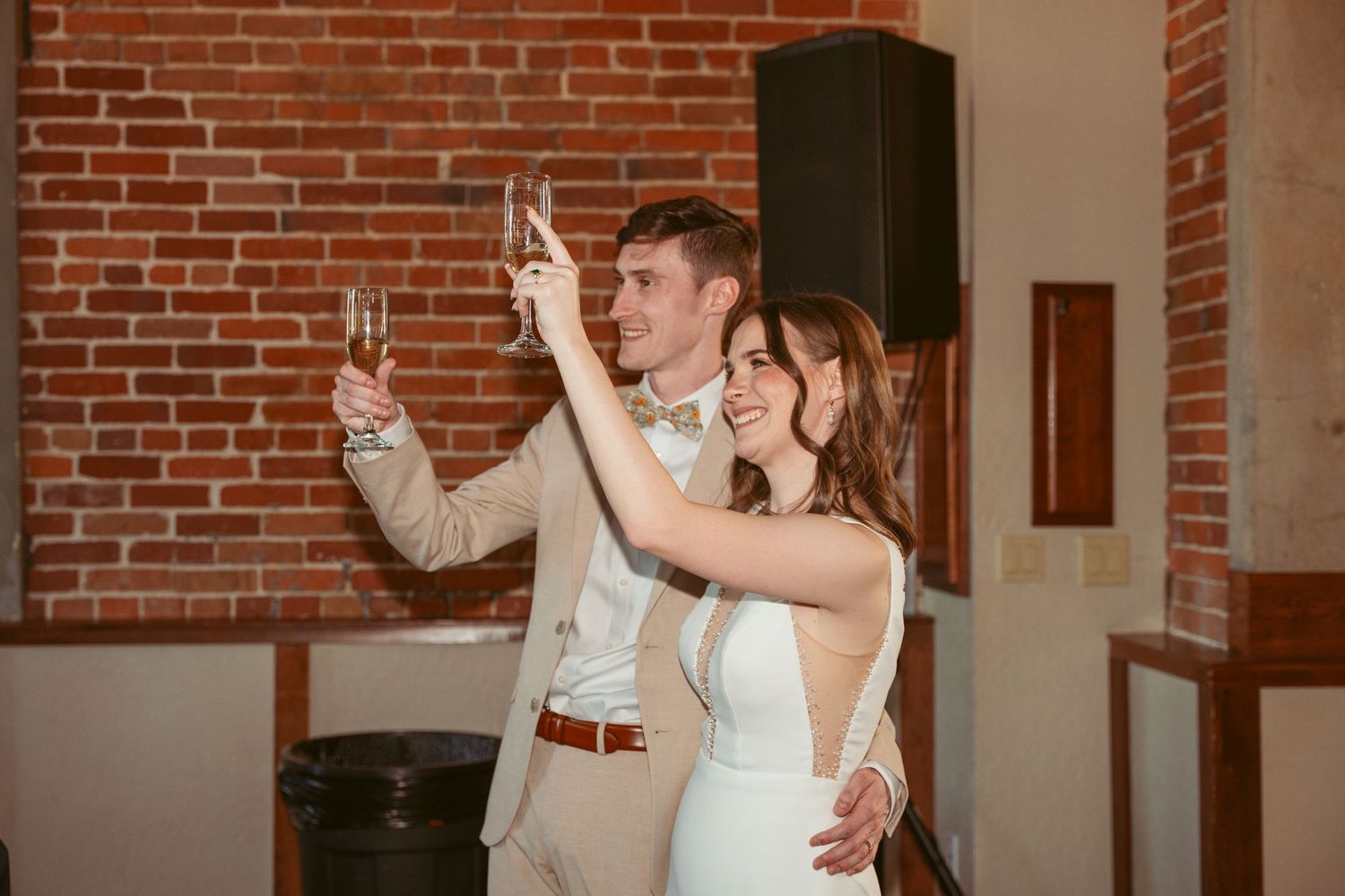 Wedding celebration with people dancing in a bright brick-walled venue.