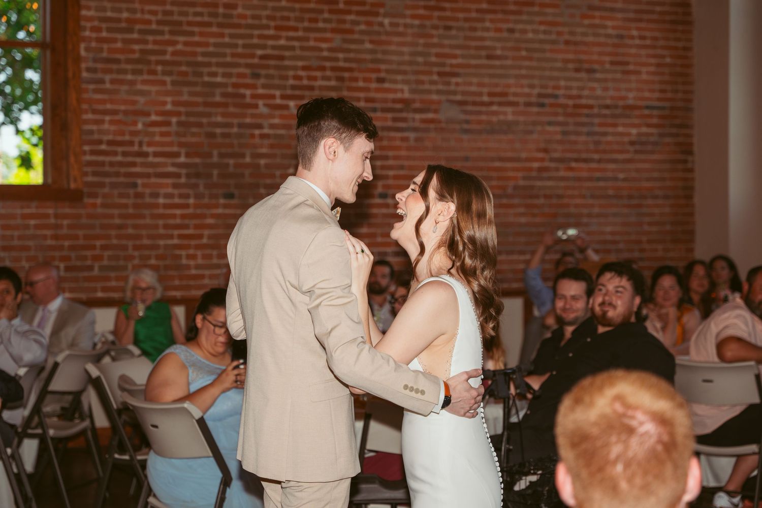 Wedding reception dance floor moment in rustic brick venue with guests watching.