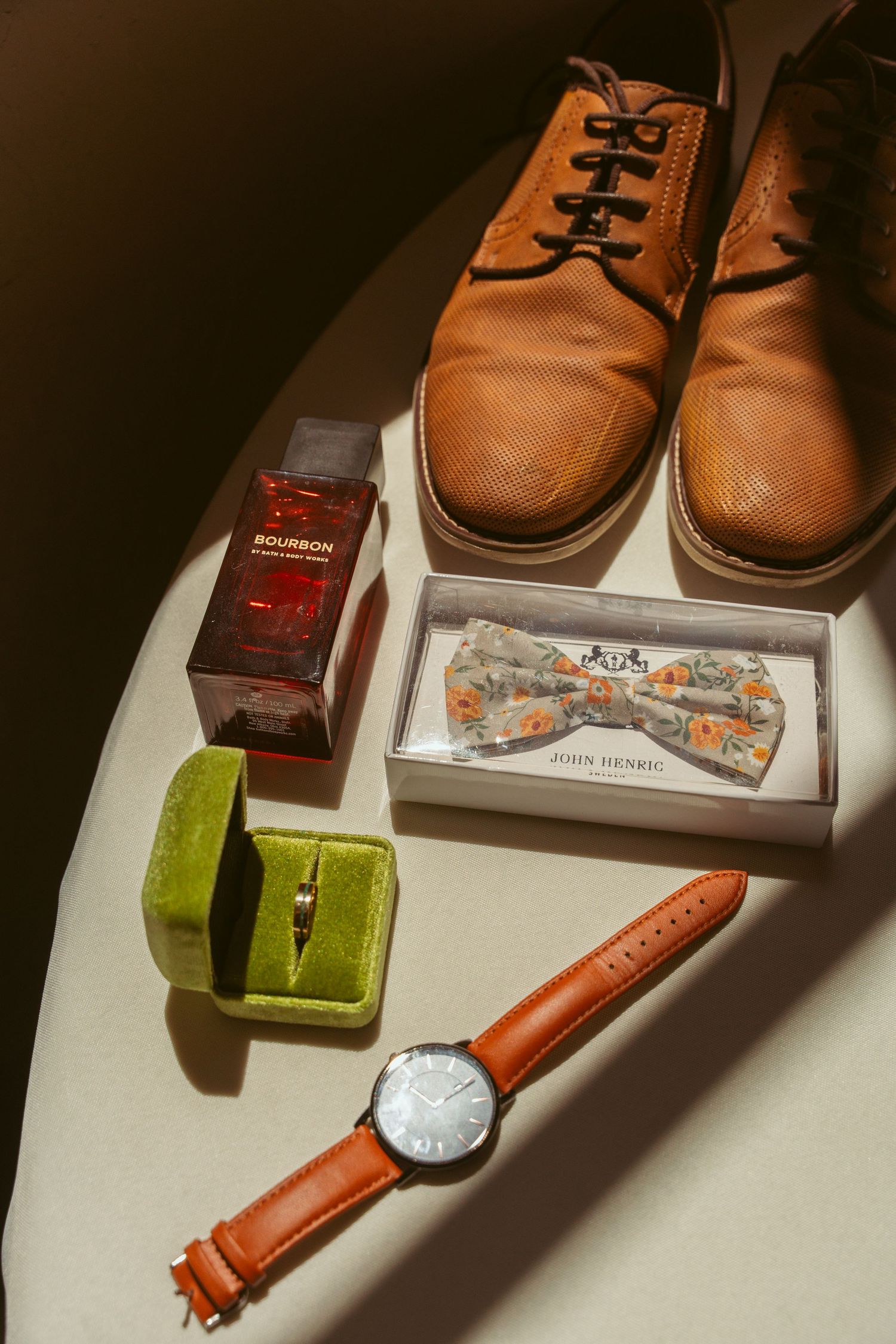 Wedding accessories including leather shoes, bow tie, and ring boxes arranged on white surface.