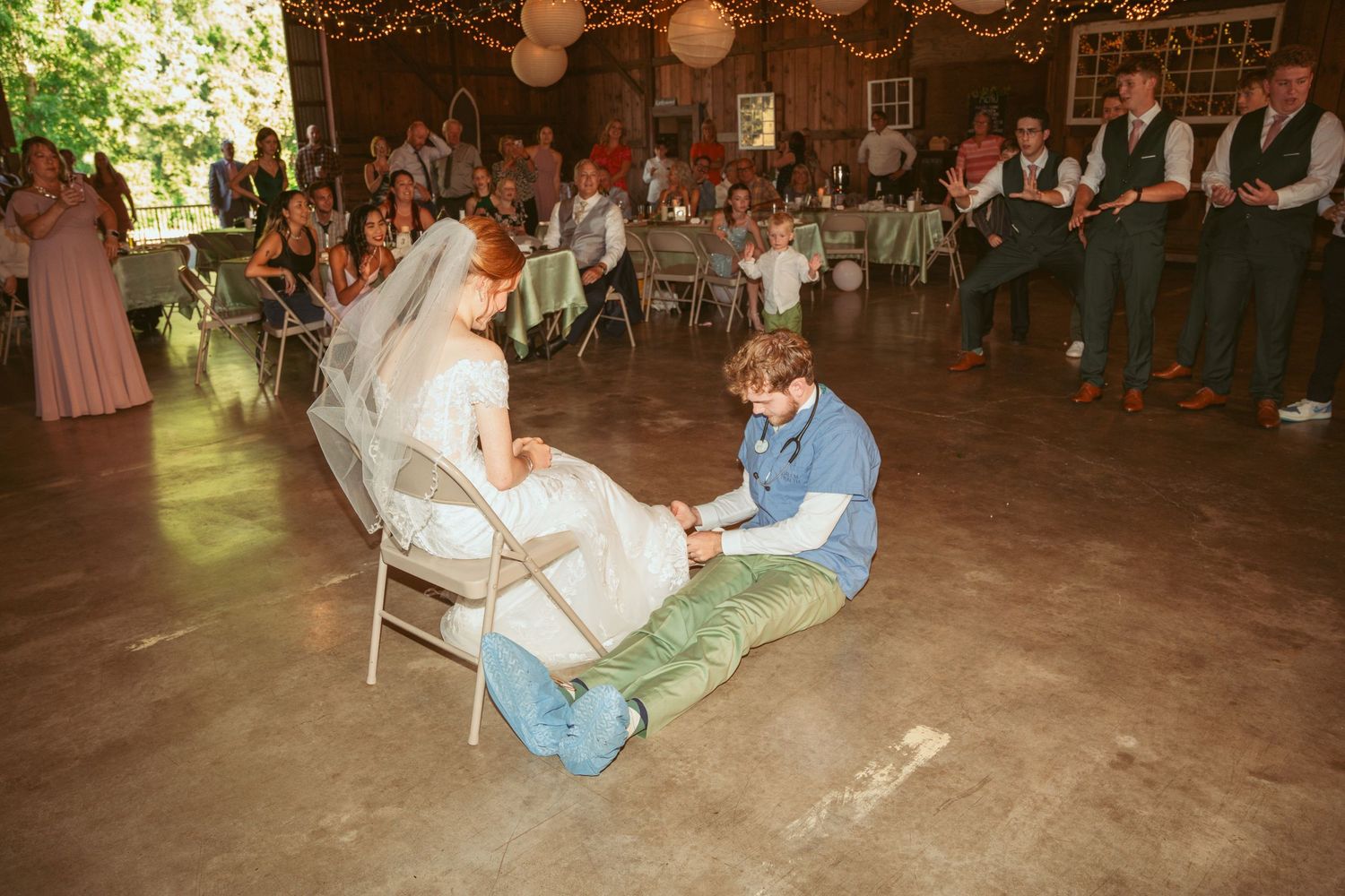 Wedding party performing a traditional garter toss ritual at a barn reception.