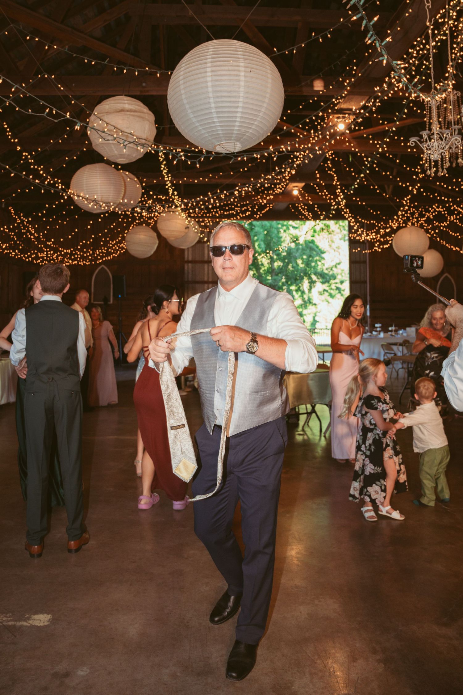 Energetic dancing at a wedding reception under twinkling lights and paper lanterns.