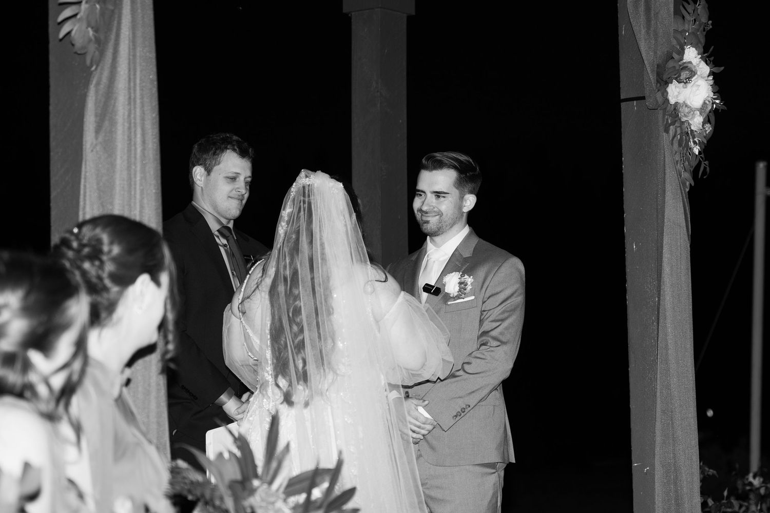 Black and white photo of a wedding ceremony under a columned pavilion with decorative draping.