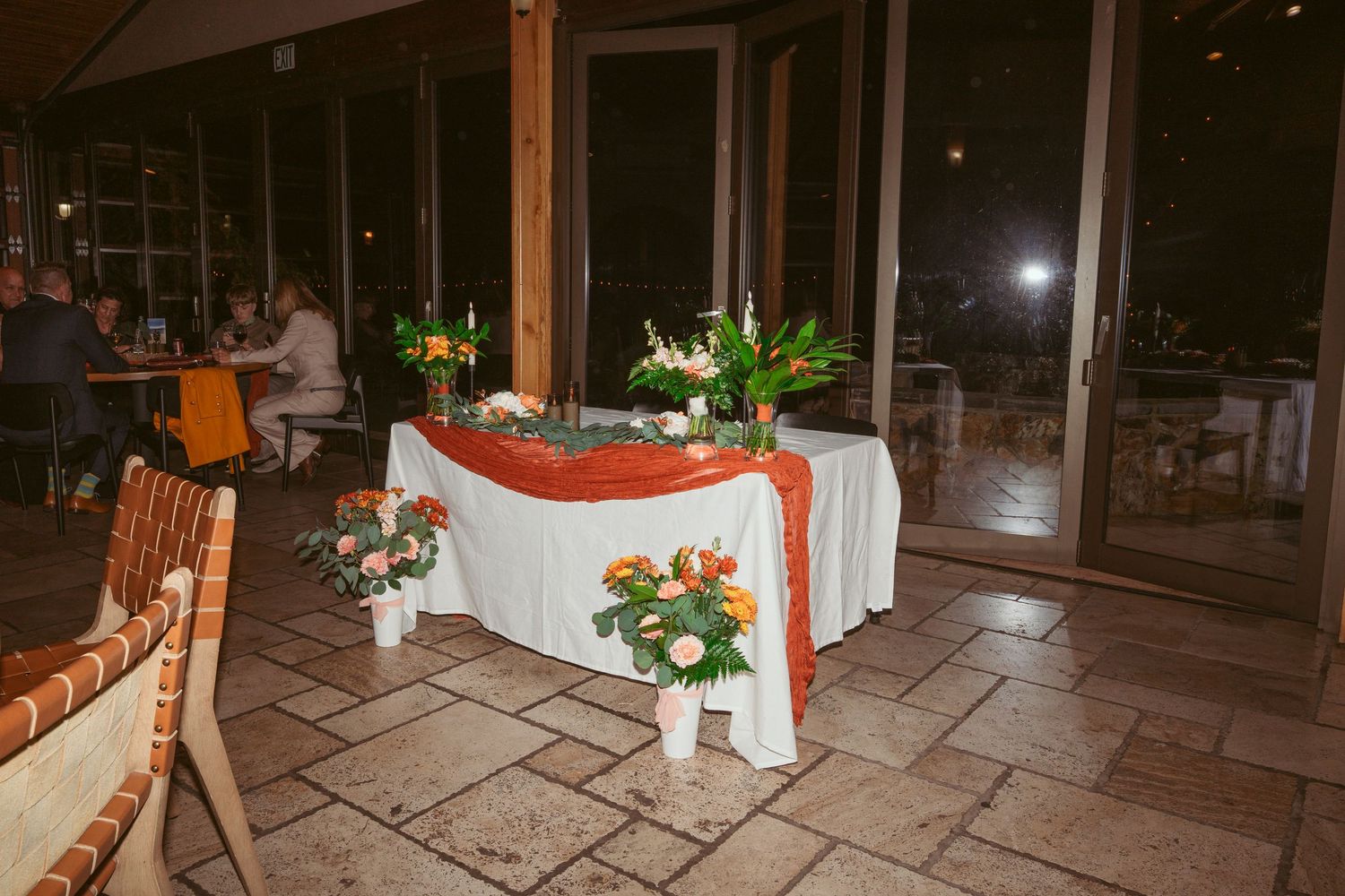 Decorated reception table with white linens and floral arrangements in evening setting.
