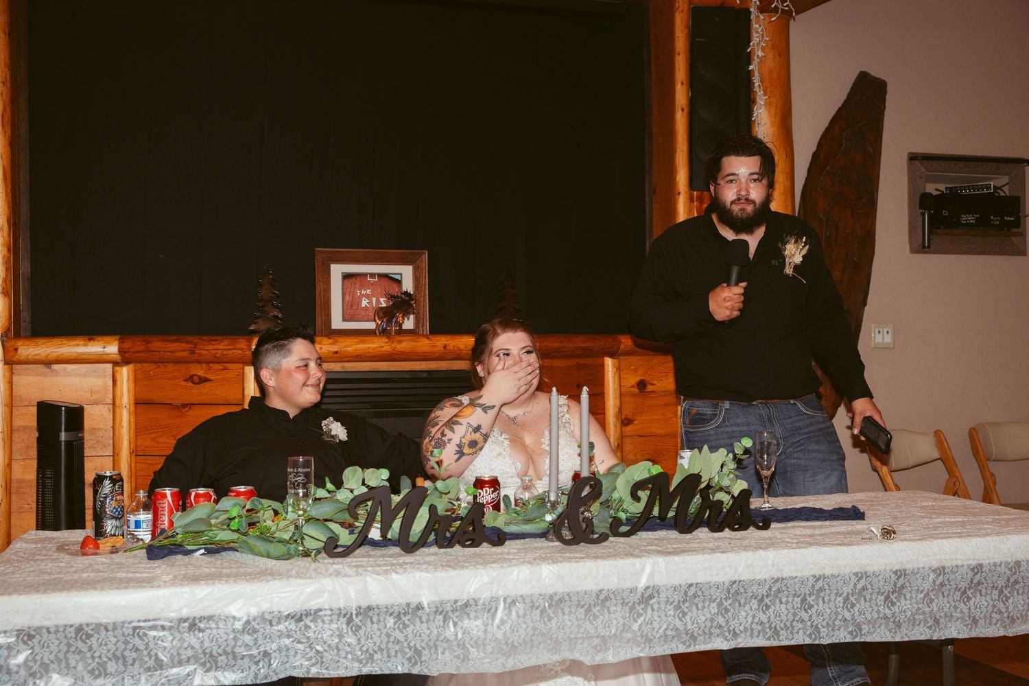 Three people gathered at a formal dinner table with one person standing and speaking to the group.