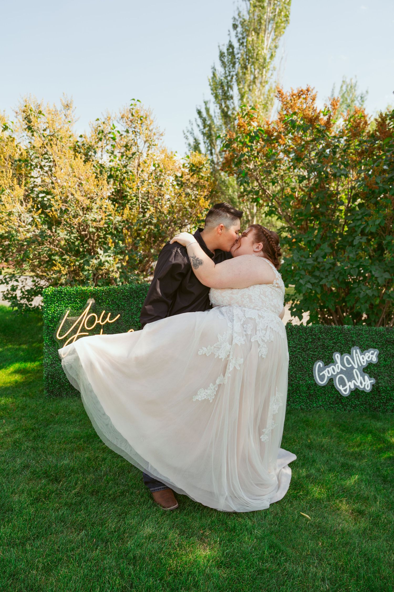 A playful wedding dip pose captured in a garden setting with golden sunlight filtering through trees.