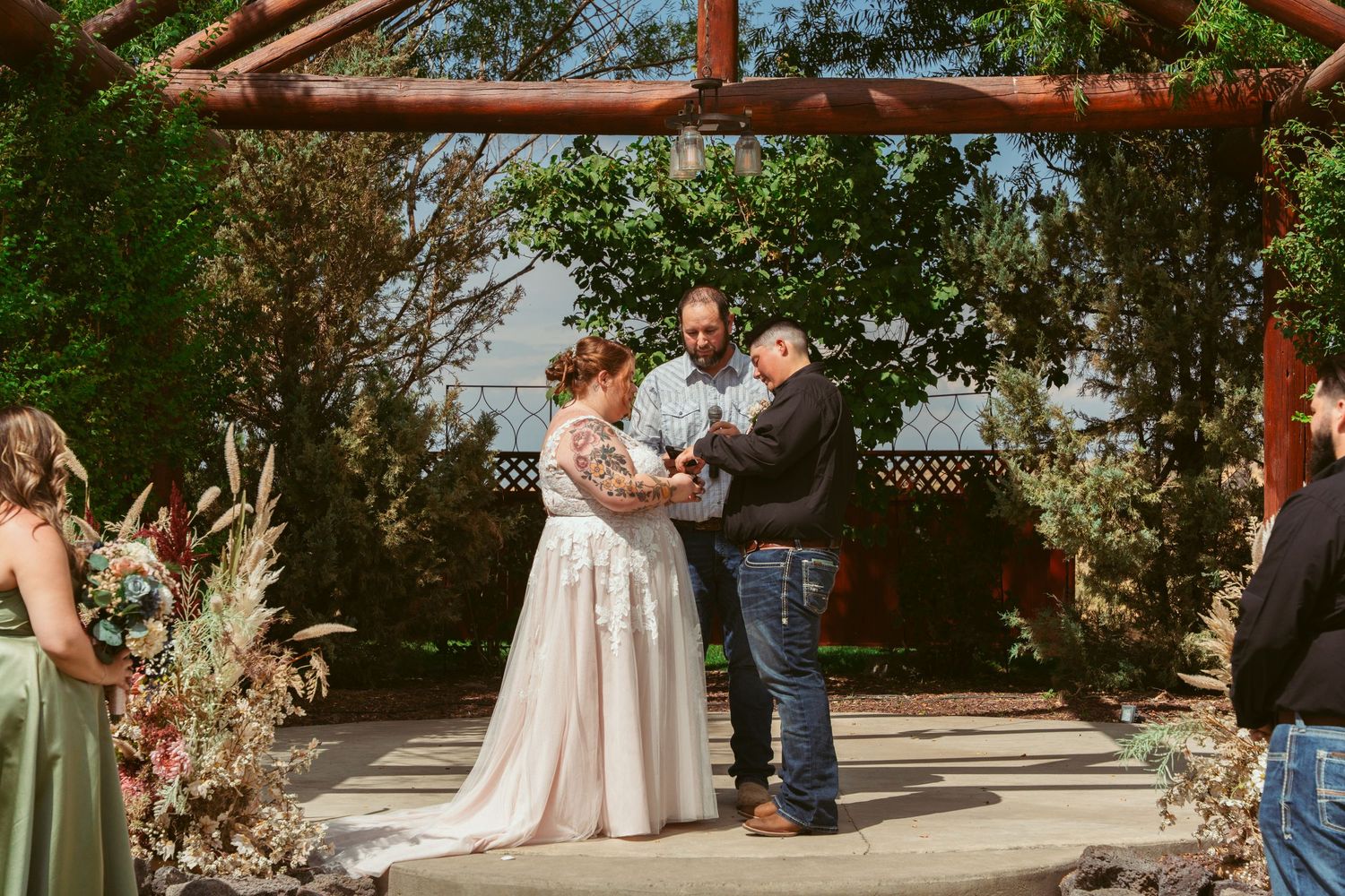 Wedding ceremony space decorated with pink flowers and wooden beams against a natural backdrop.