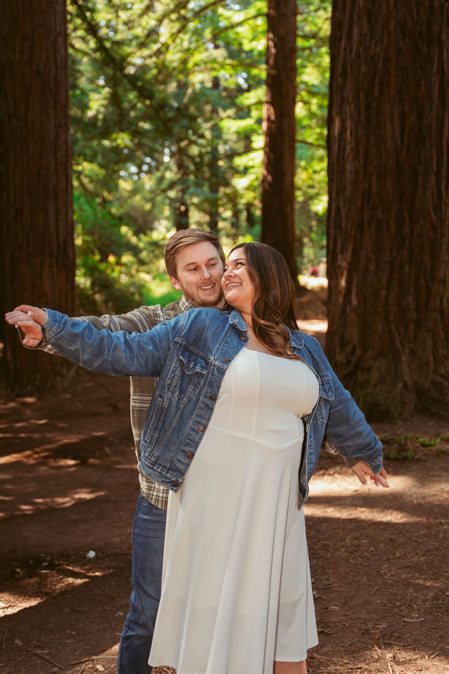 A playful couple spreads their arms wide while enjoying a moment in the redwood forest.