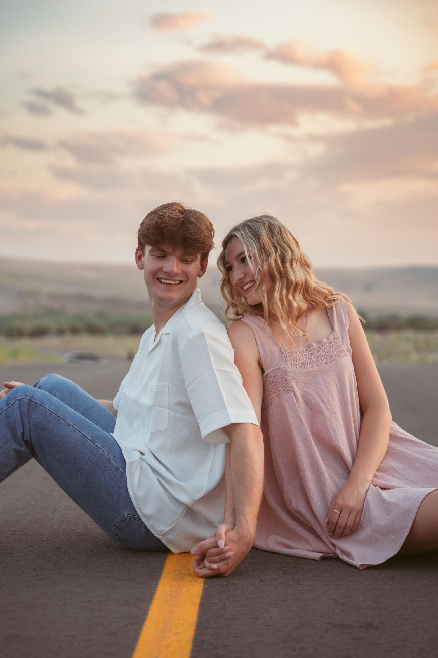 A couple sits together on a yellow road line during golden hour.