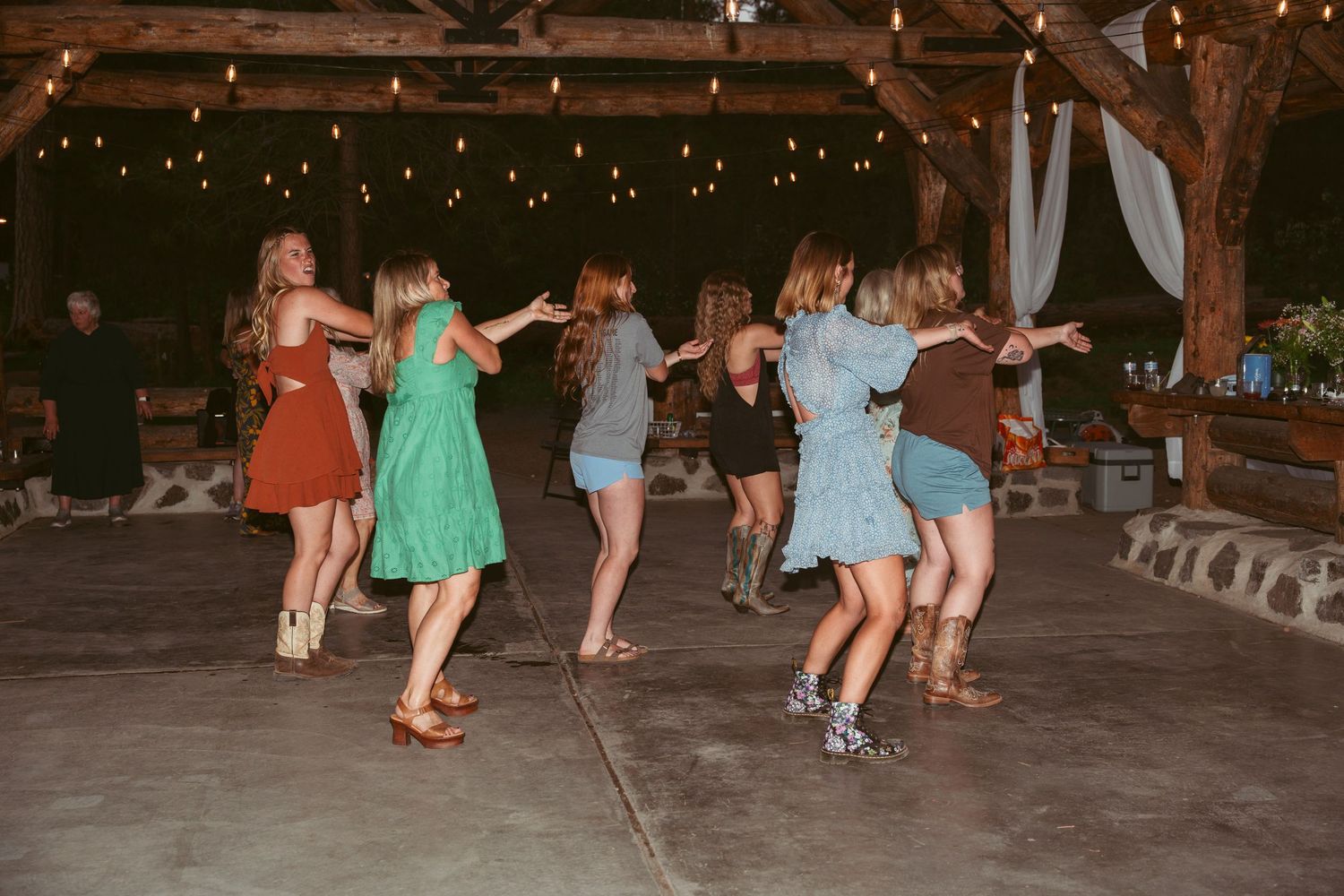 Wedding guests dance in groups on a covered outdoor dance floor during evening reception.