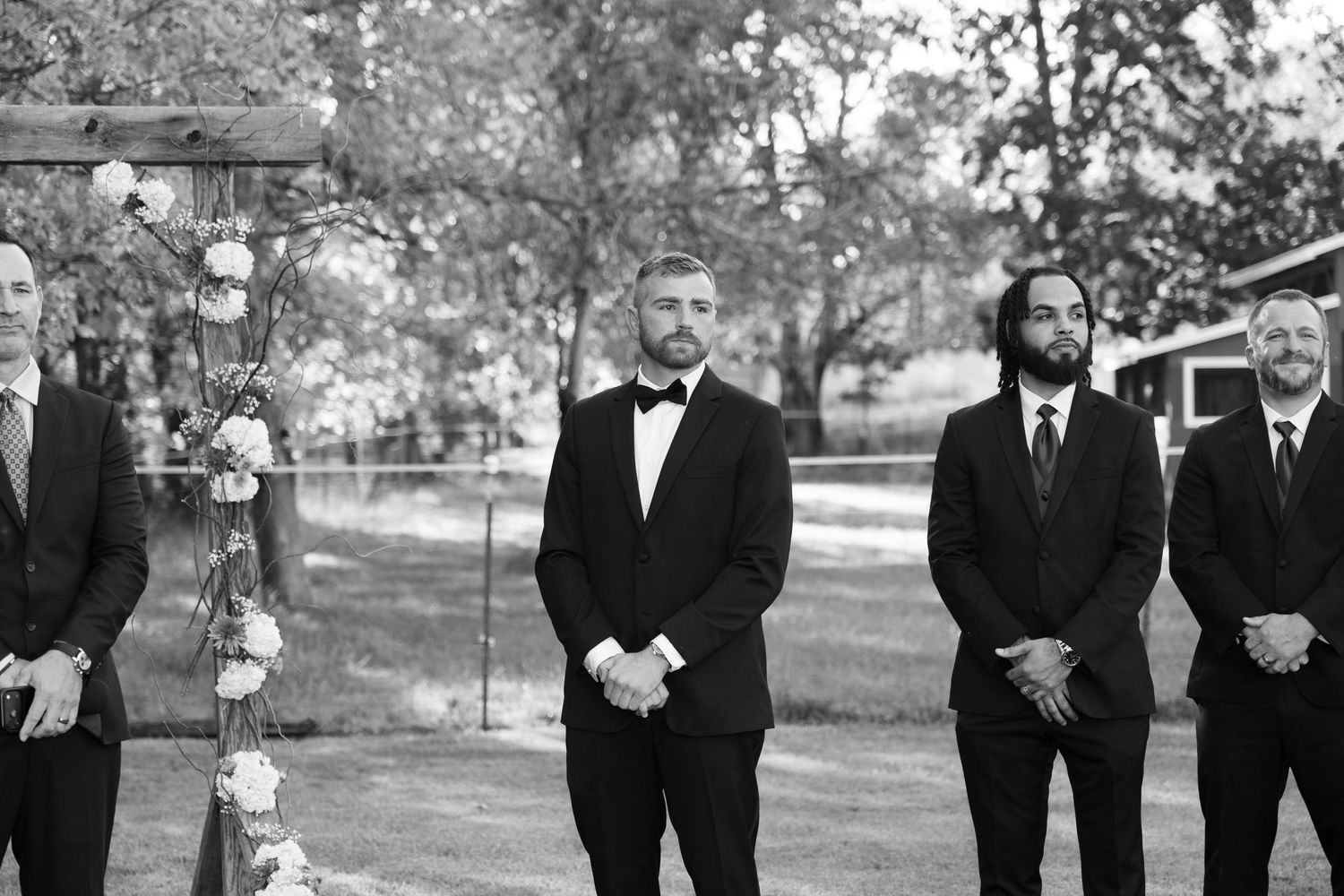 Black and white photo of groomsmen in formal attire standing outdoors.