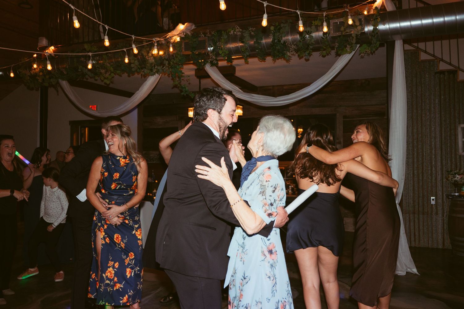 Couples dancing together at an indoor event venue with string lights hanging from the ceiling.