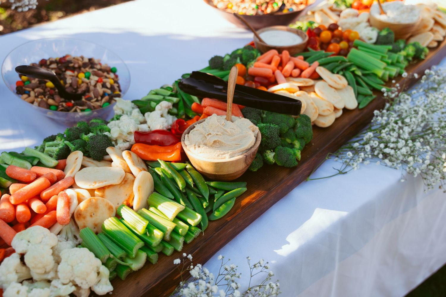 Fresh vegetable and appetizer platter with carrots, cucumbers, and dips arranged on wooden board.