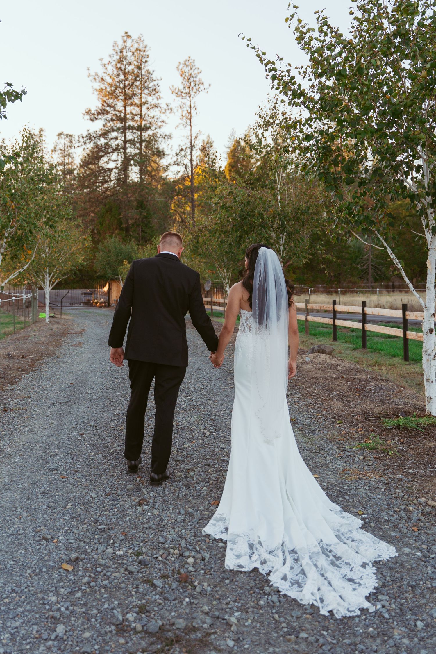 Newlywed couple walking on a gravel path surrounded by autumn trees.