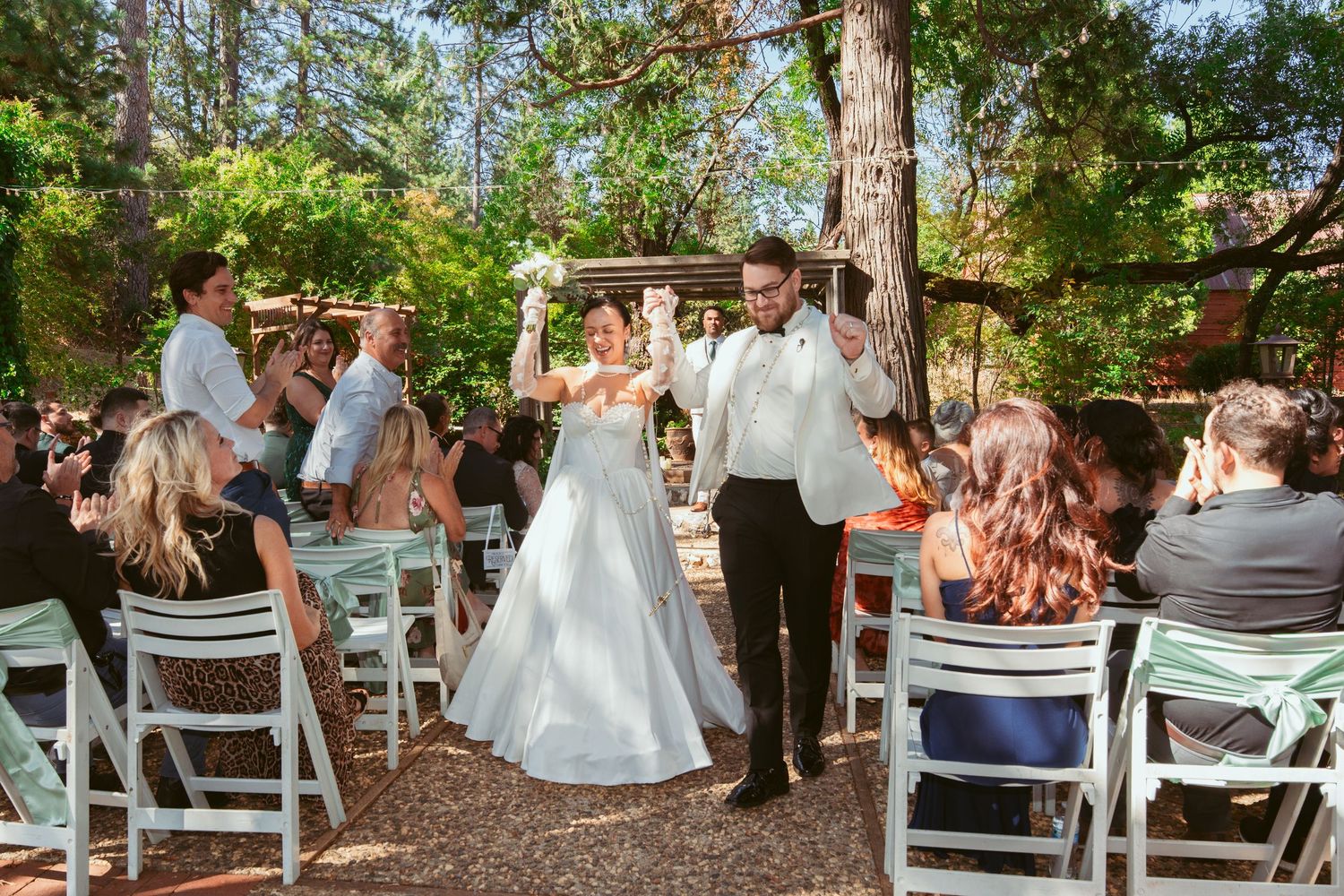 Outdoor wedding ceremony setup with white chairs among pine trees.