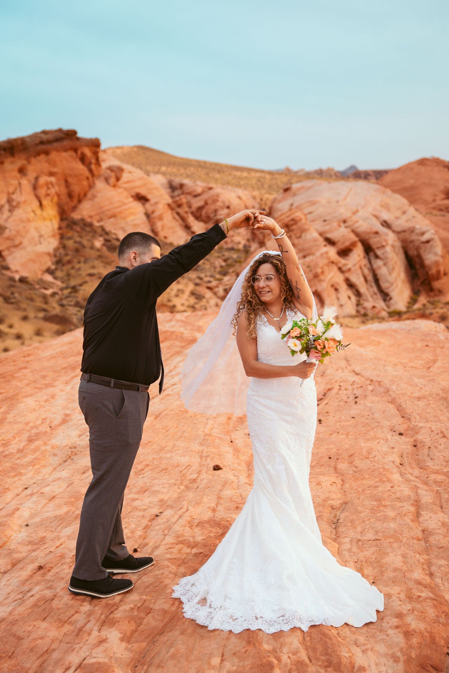 A couple dances and poses playfully on red rock formations during their desert wedding photoshoot.