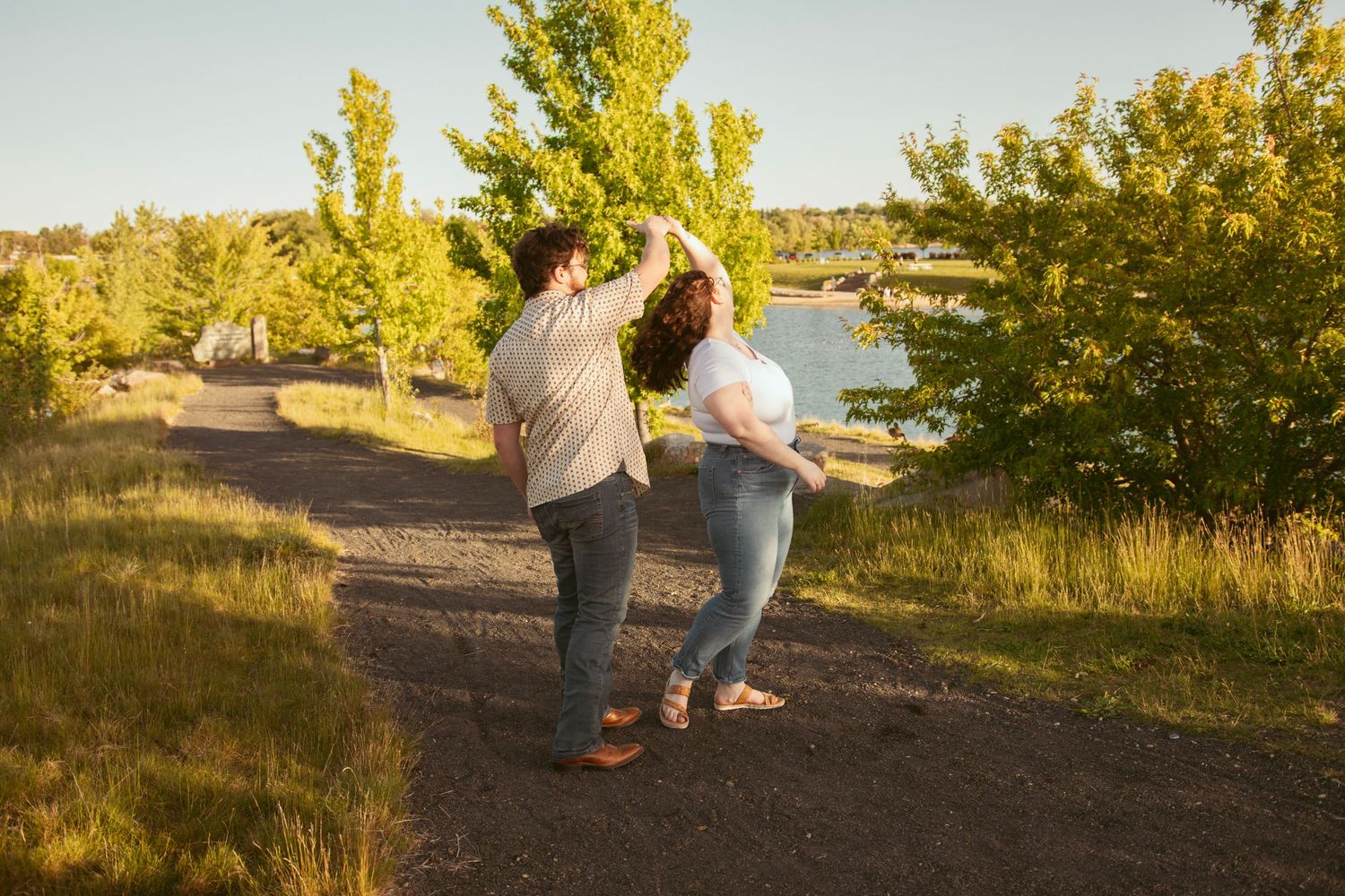 A couple walks together on a dirt path surrounded by yellow trees at sunset.