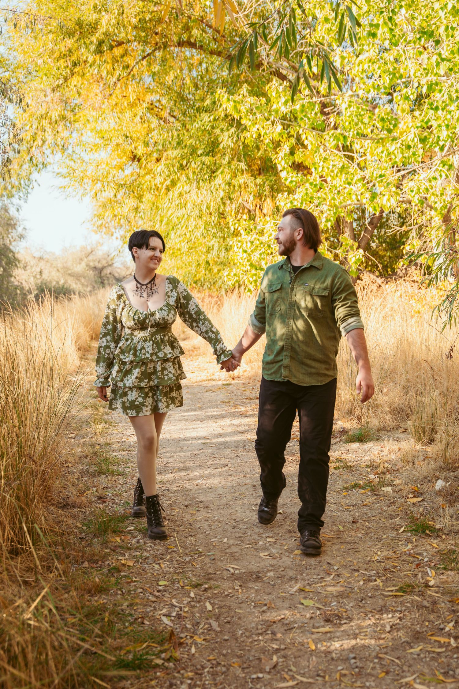Couple runs playfully through autumn trees on nature trail.