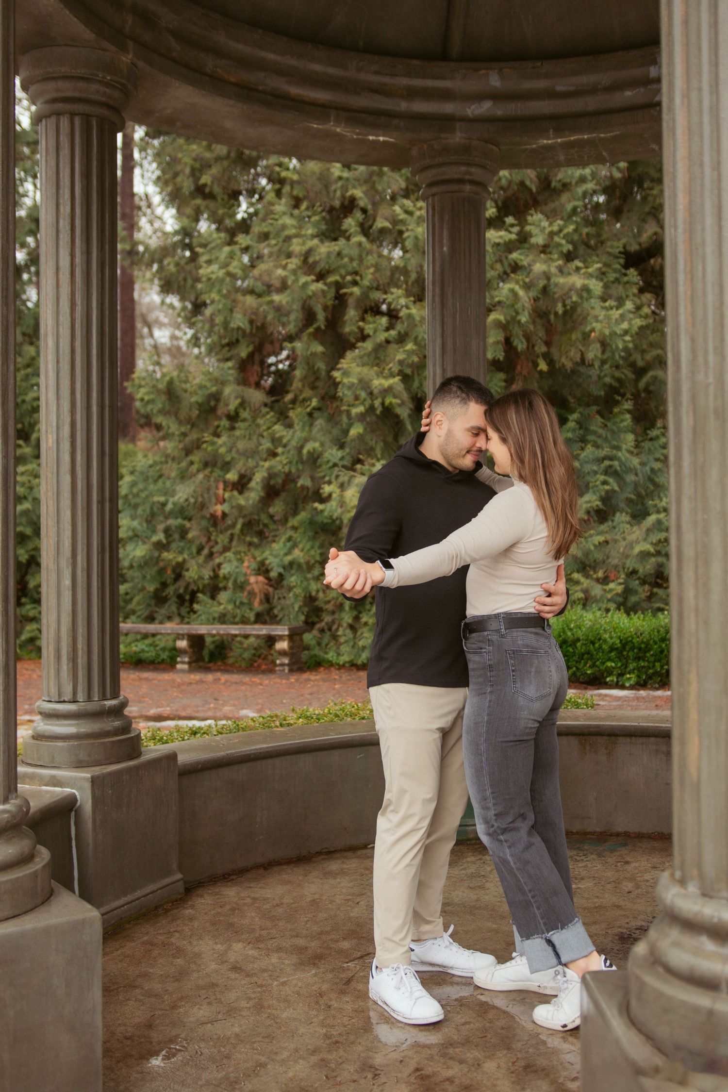 A couple dancing together in a stone gazebo surrounded by lush gardens.