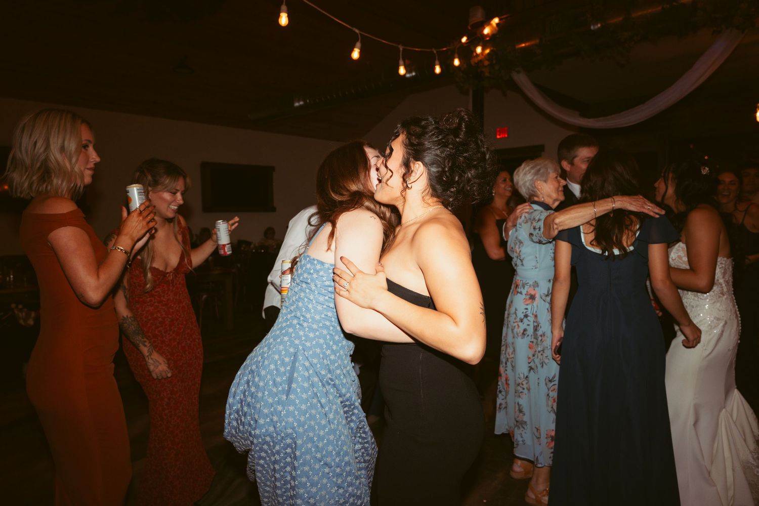 Party guests dancing together under string lights at an indoor evening celebration.