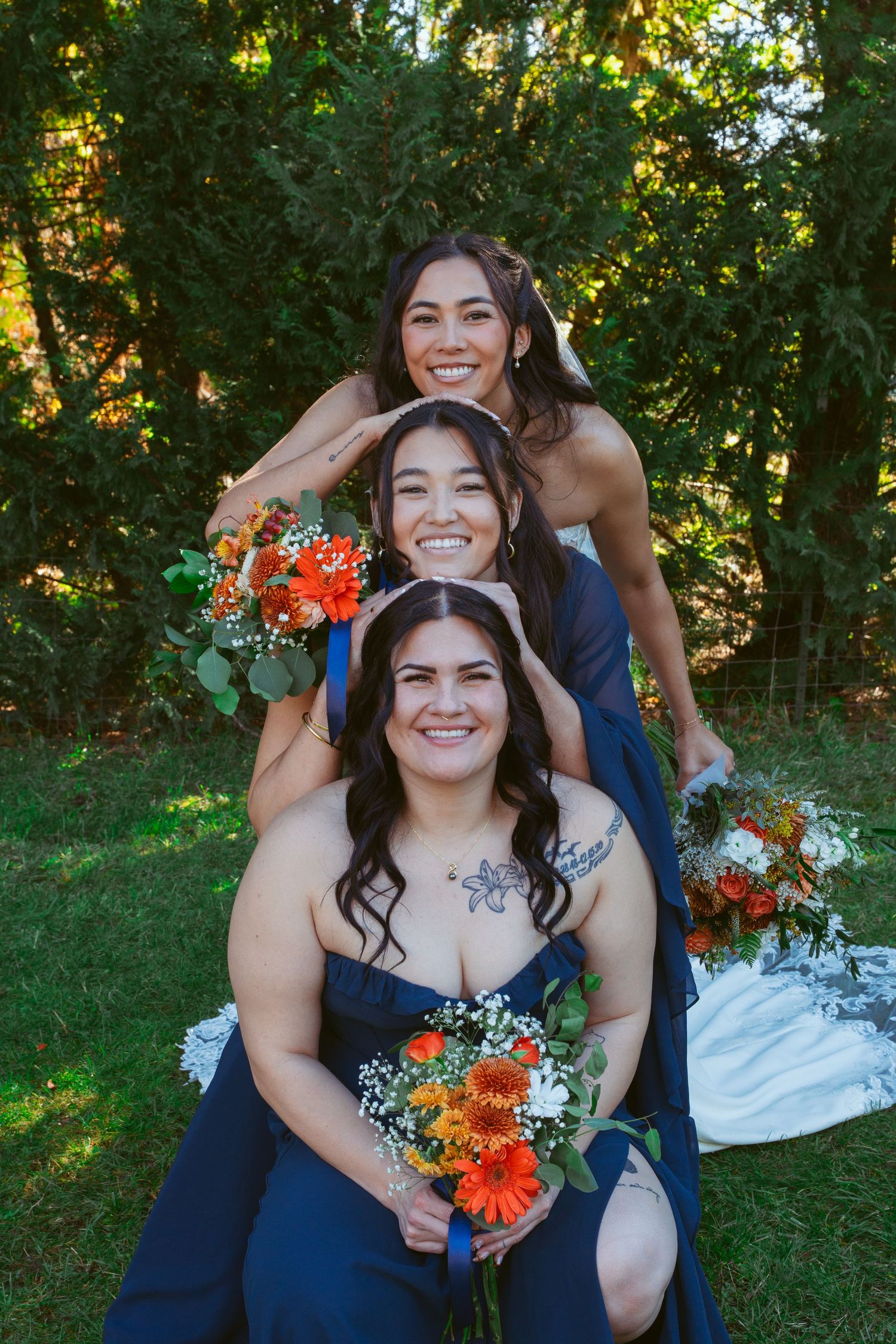 Bridesmaids in navy dresses hold orange bouquets while smiling outdoors.