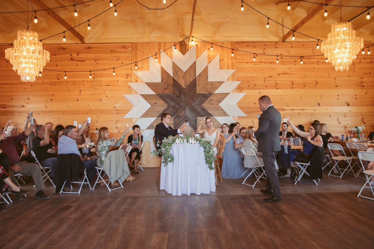 A rustic barn wedding reception venue with string lights and crystal chandeliers.