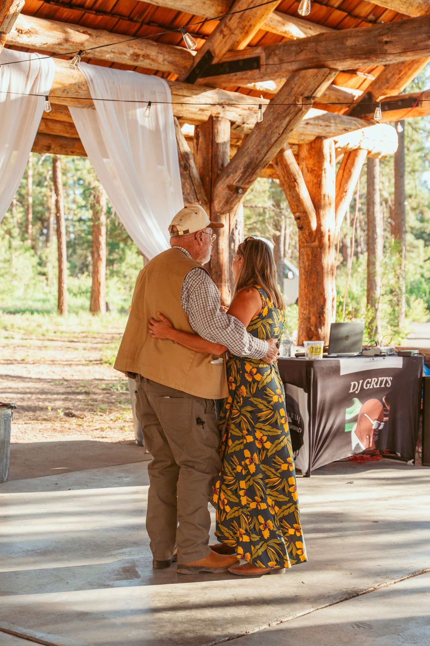 Couples dance under a rustic wooden pavilion with DJ equipment visible.