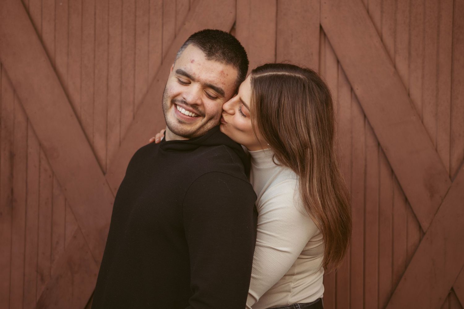 Couple sharing intimate moments against a rustic brown barn door background.