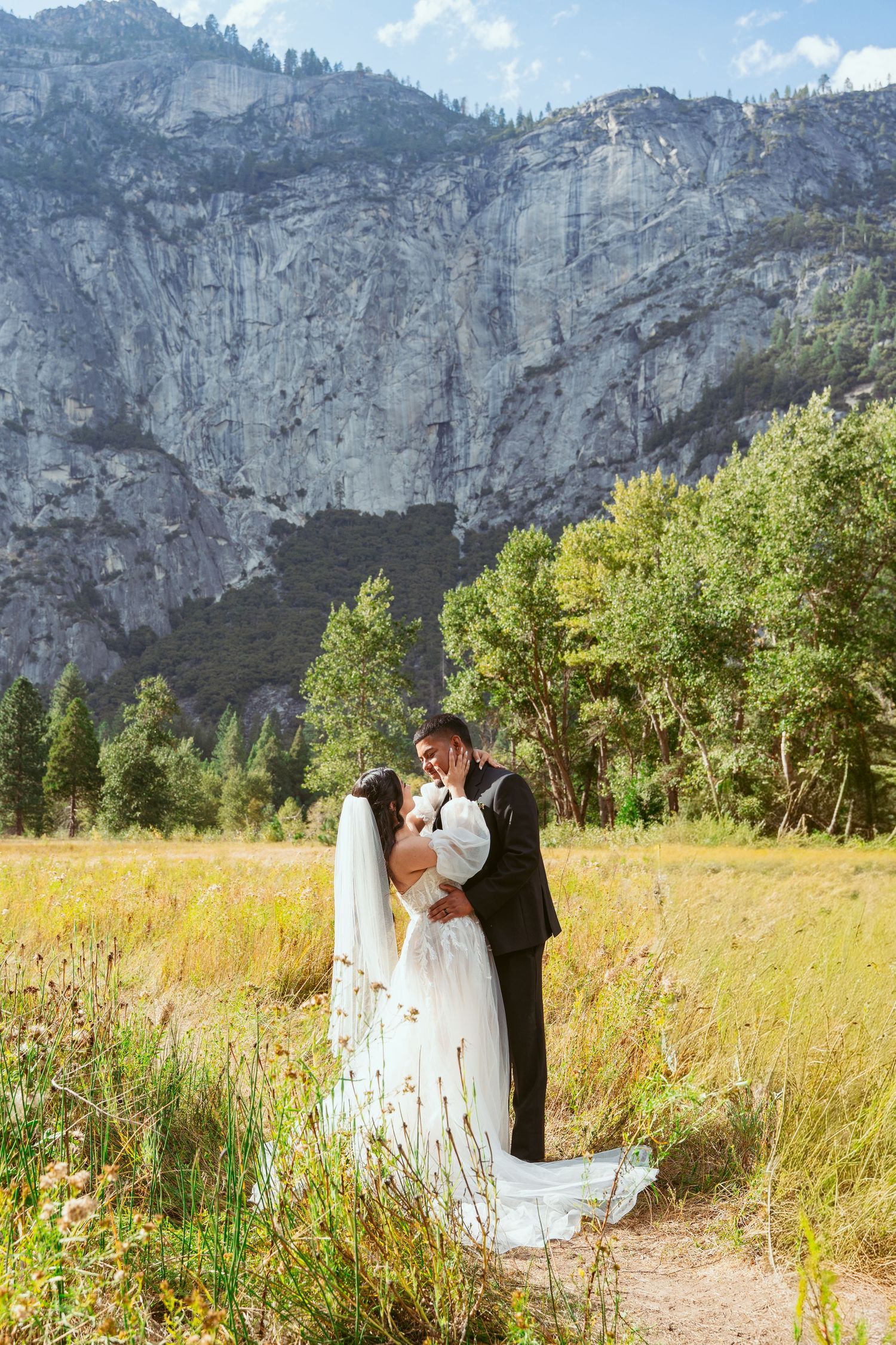 Wedding couple embracing in a meadow beneath Yosemite's towering granite walls.