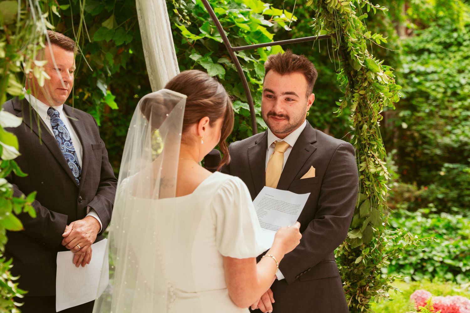 Outdoor wedding ceremony with elegant white draping and natural greenery as backdrop.