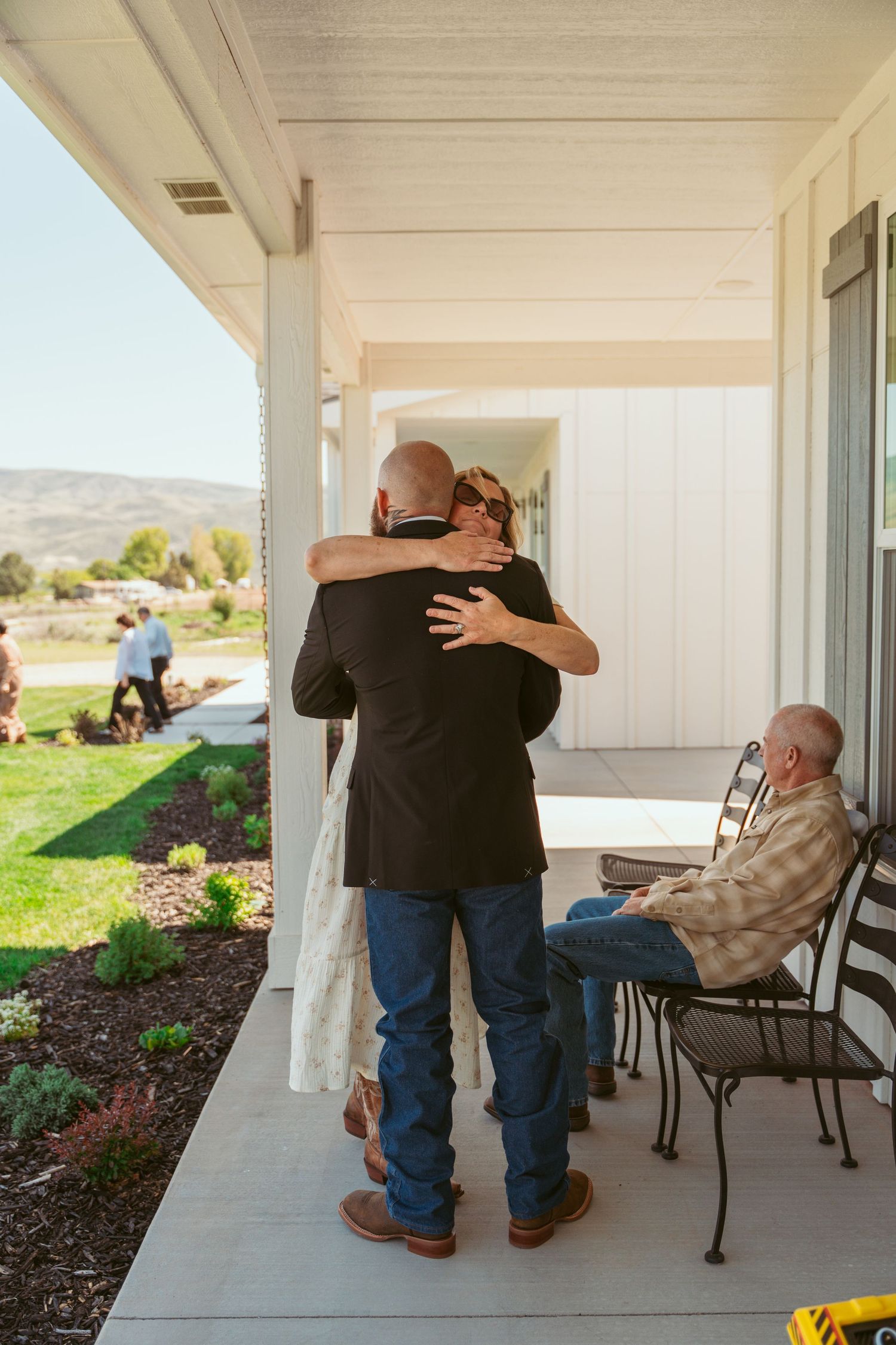 People embrace on a covered porch with outdoor furniture and mountain views.