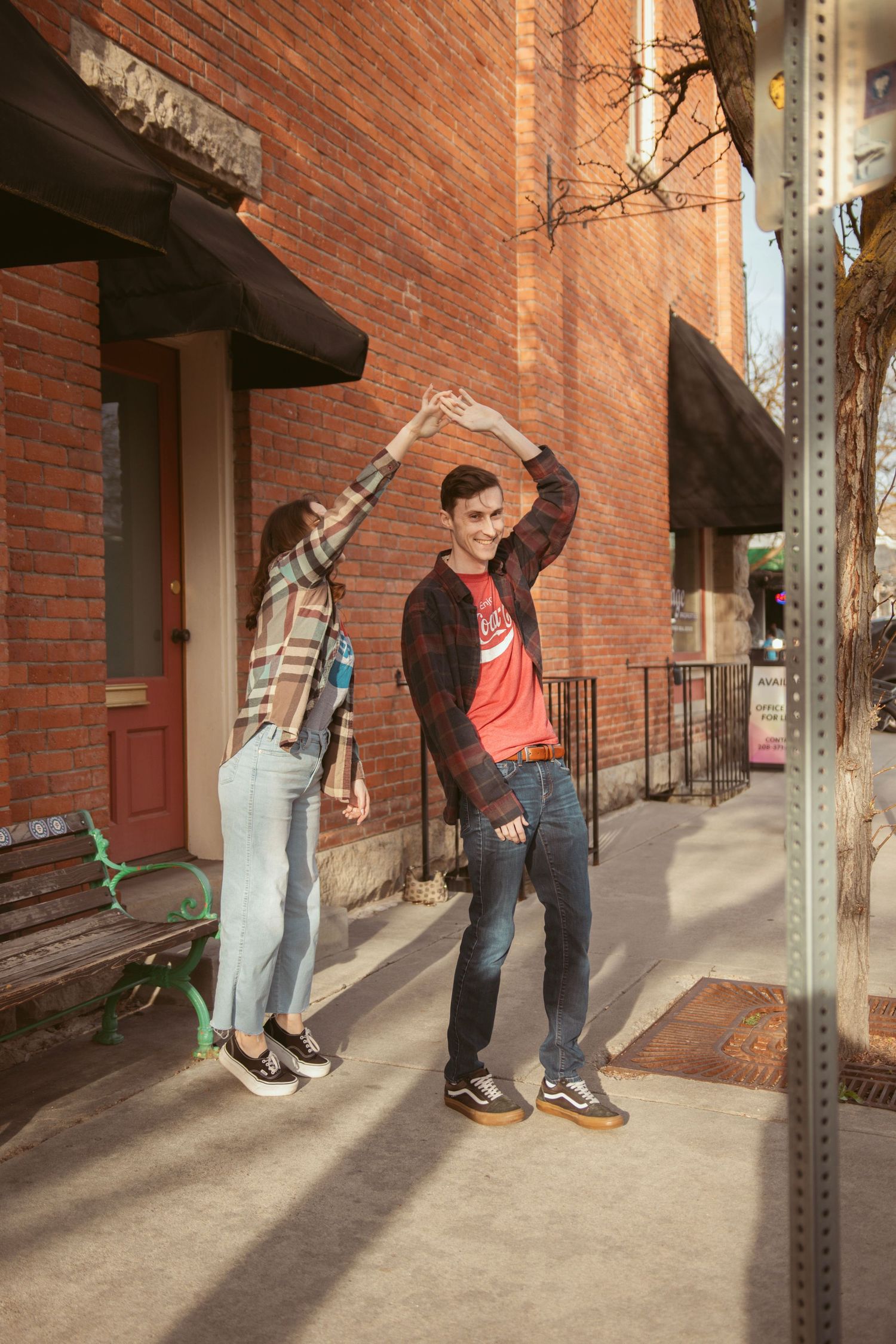 Two people perform synchronized dance moves on a city sidewalk next to a brick building.