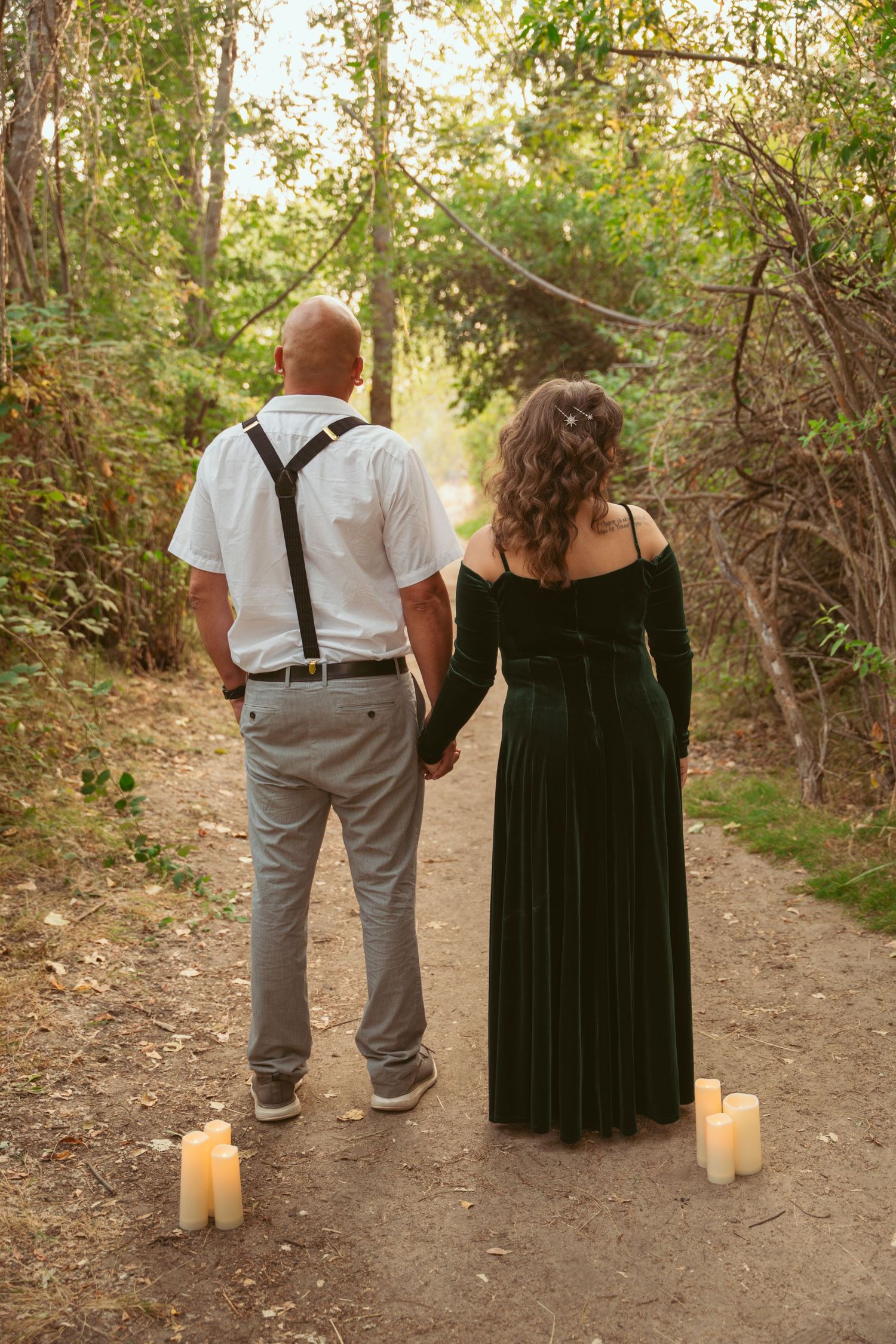 Couple walking on a candlelit nature path with warm evening light filtering through trees.