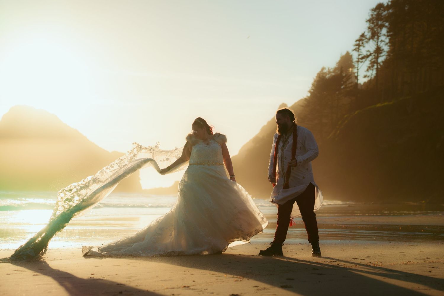 Dramatic wide-angle beach scene with couple and flowing dress against setting sun.