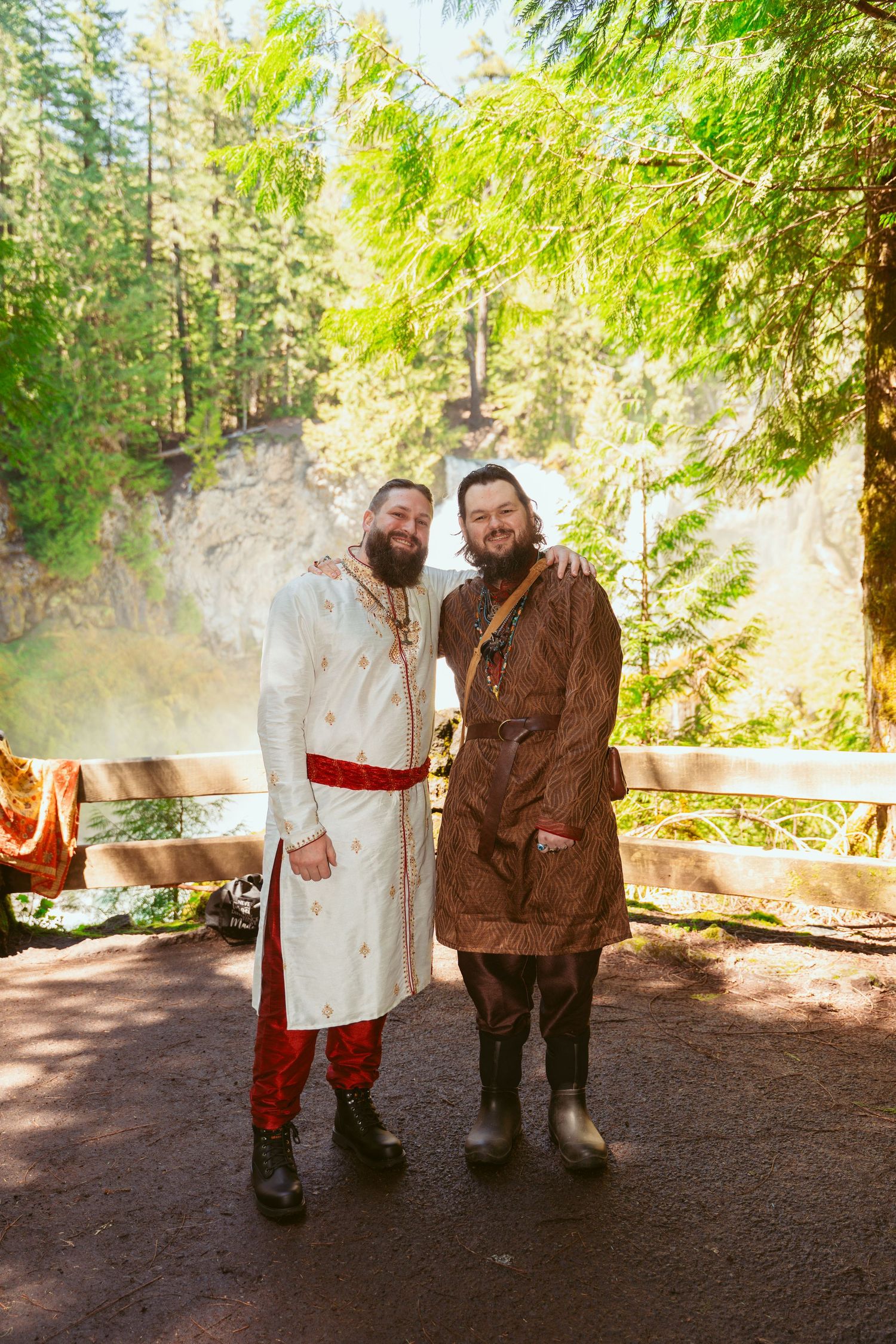 A couple in medieval-themed wedding clothing poses together on a forest path.