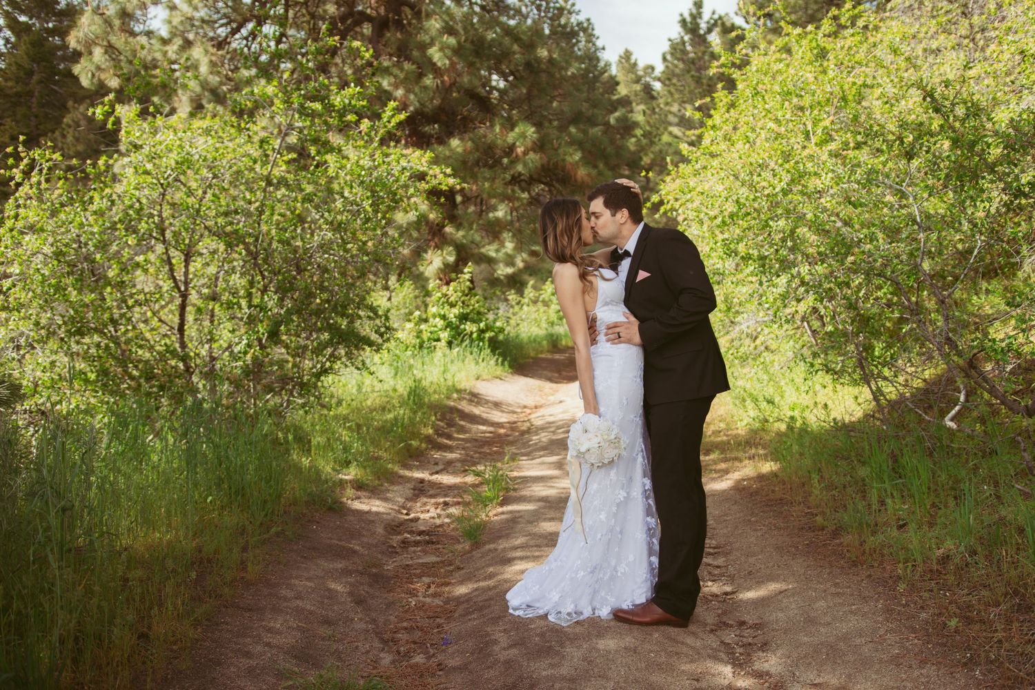 Newlyweds share an intimate moment on a tree-lined dirt path.
