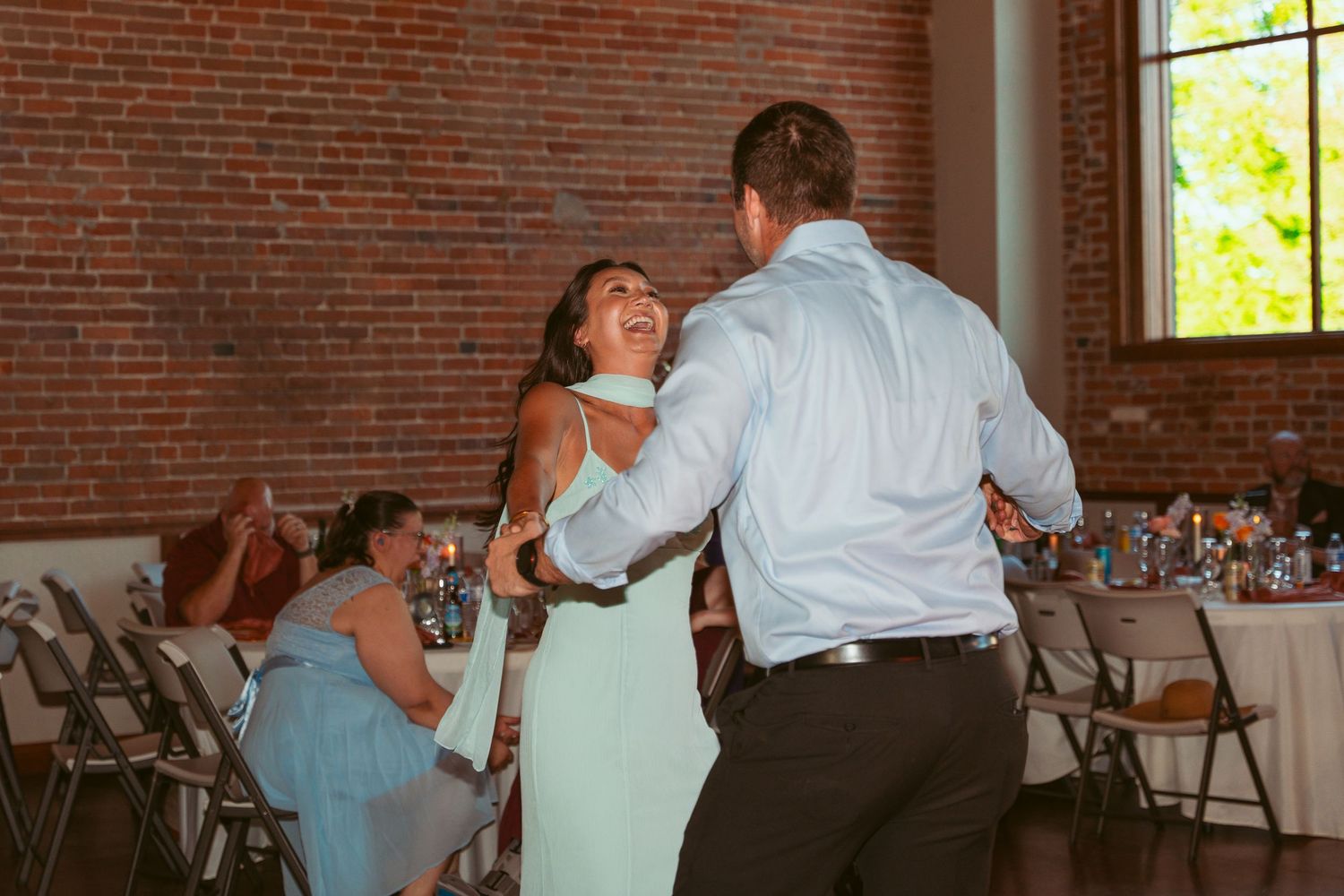 Guests enjoying group dances at a wedding reception in a historic brick building with string lights.