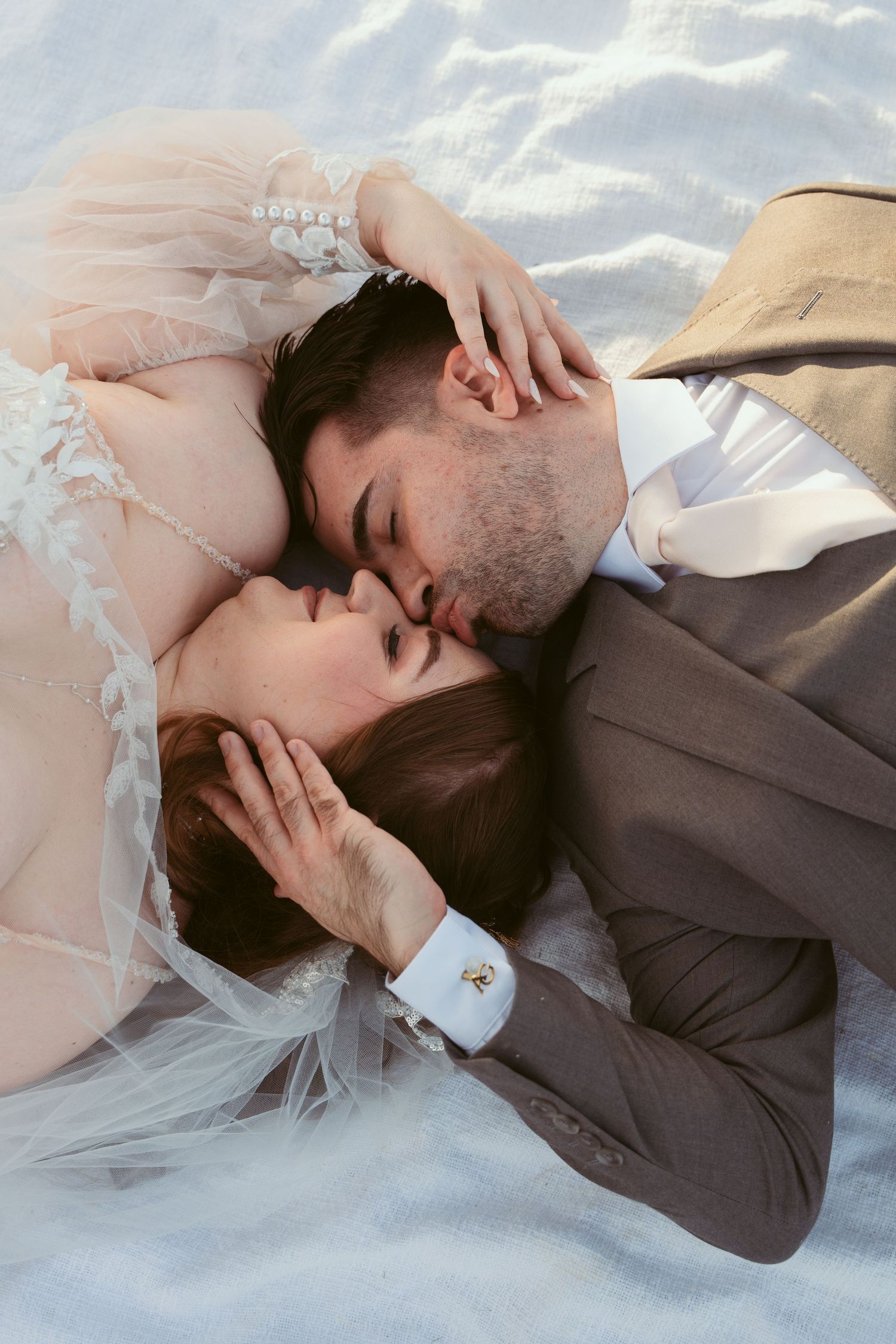 Intimate wedding moment captured on white fabric with soft lighting.