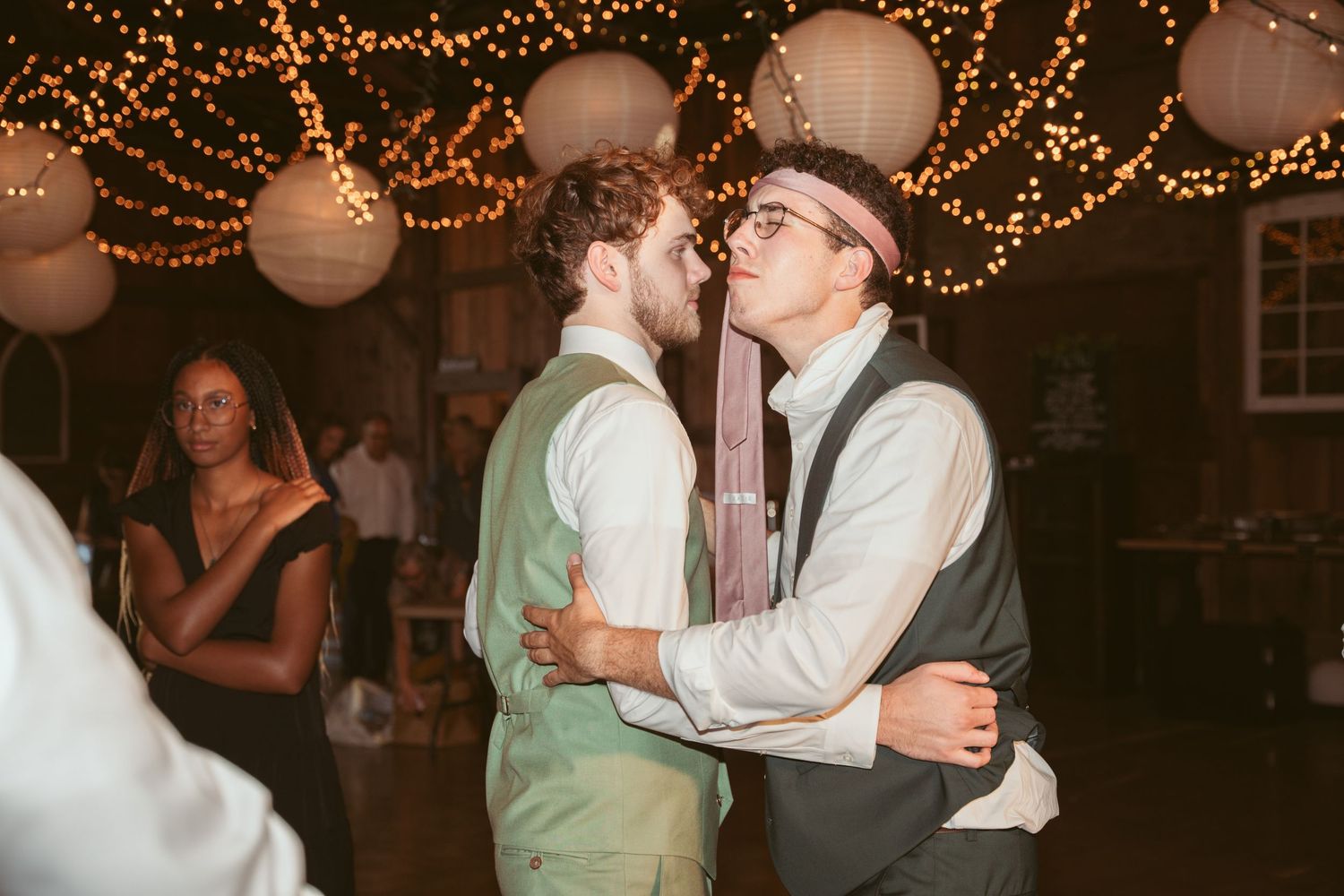 Wedding reception dance floor with guests celebrating under romantic string lighting.