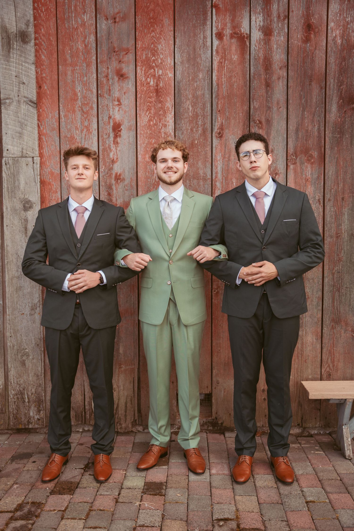 Formal group photo of wedding party members standing together against weathered barn siding.
