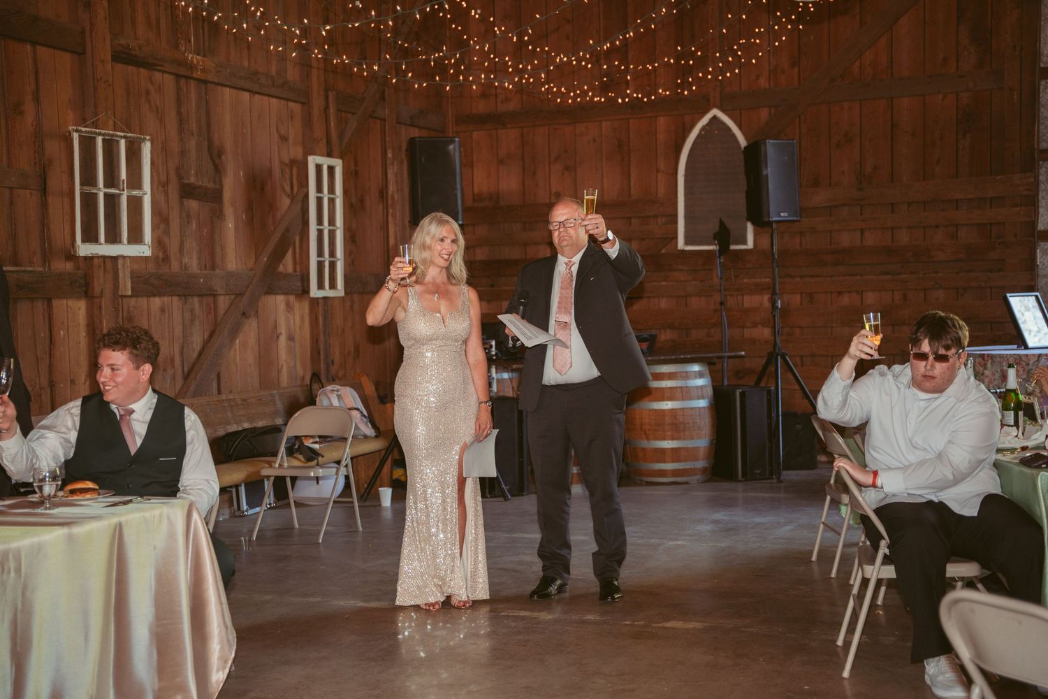 Rustic barn wedding reception with string lights and white paper lanterns decorating the wooden ceiling.