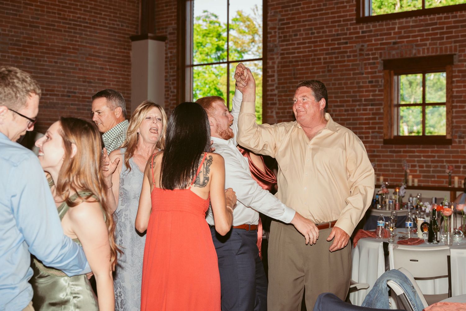 Wedding reception guests mingle and dance in a rustic brick venue with string lights.
