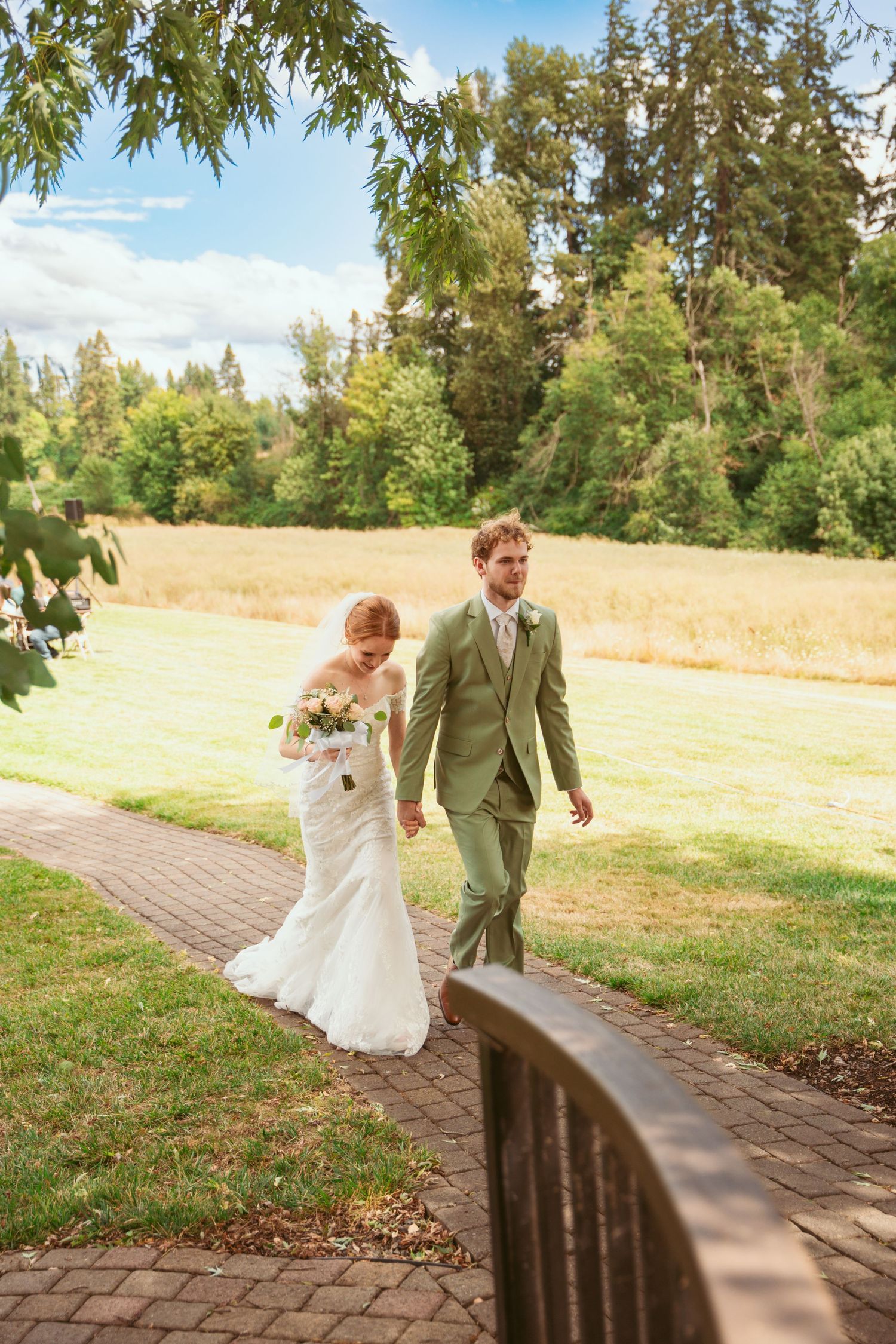 A winding brick pathway leads through a grassy area with trees and golden fields in the background.
