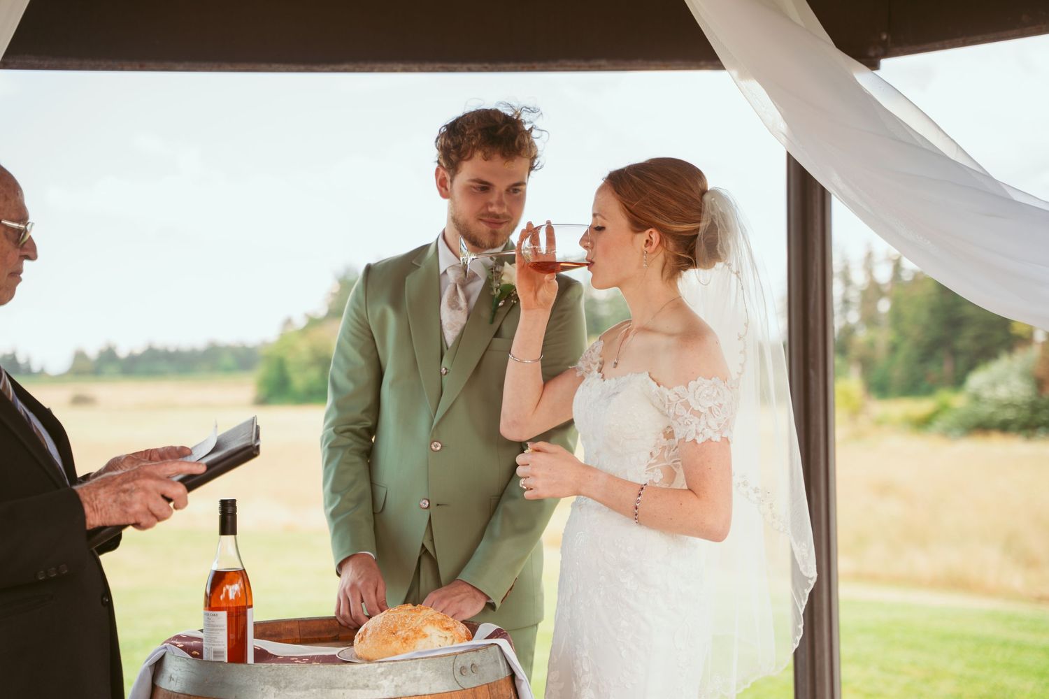 Wedding couple shares intimate moment during ceremony under wooden pavilion with white draping.