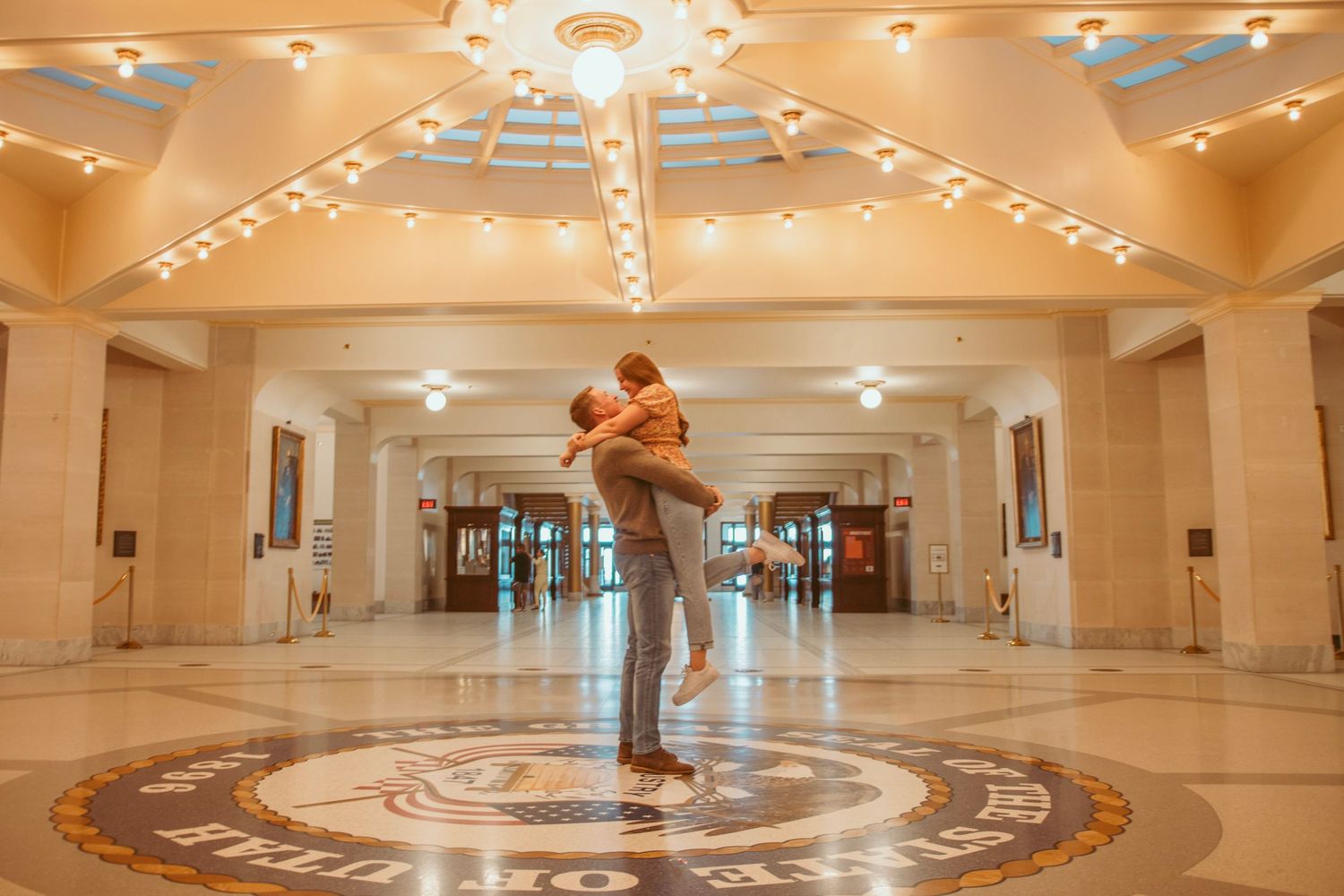 A couple dances together in an elegant ballroom with ornate lighting and patterned floor.