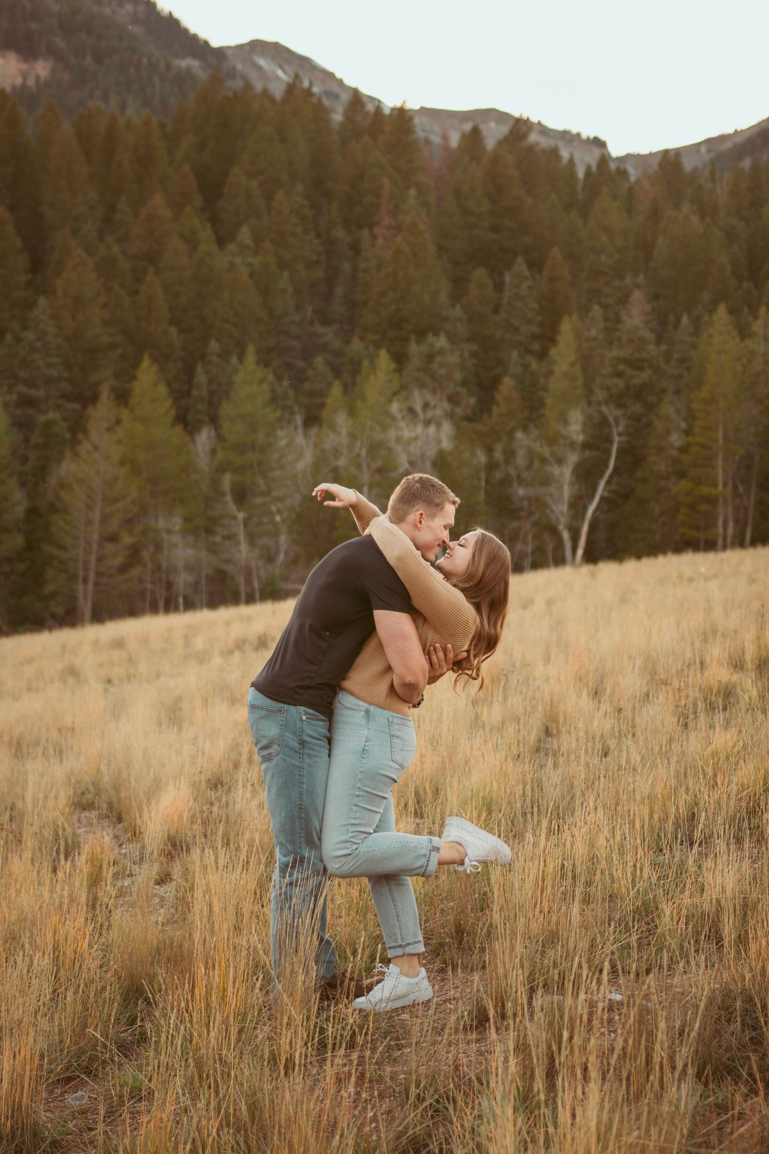 Intimate moment captured between couple in mountain meadow at sunset.