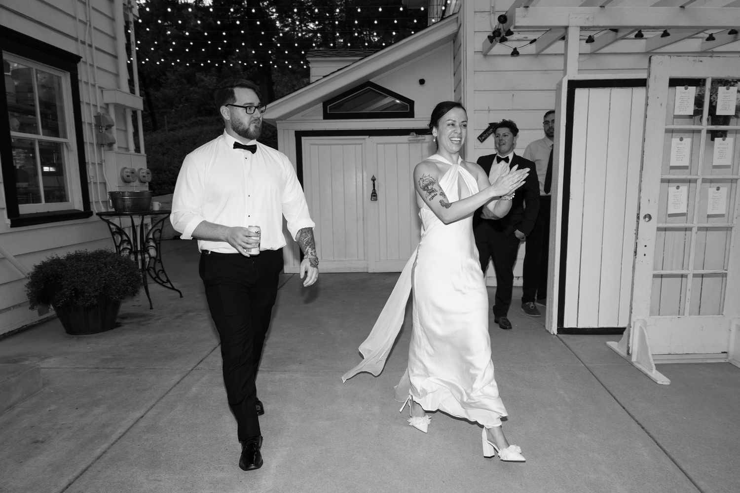Black and white photo of couples dancing at a wedding reception with string lights overhead.