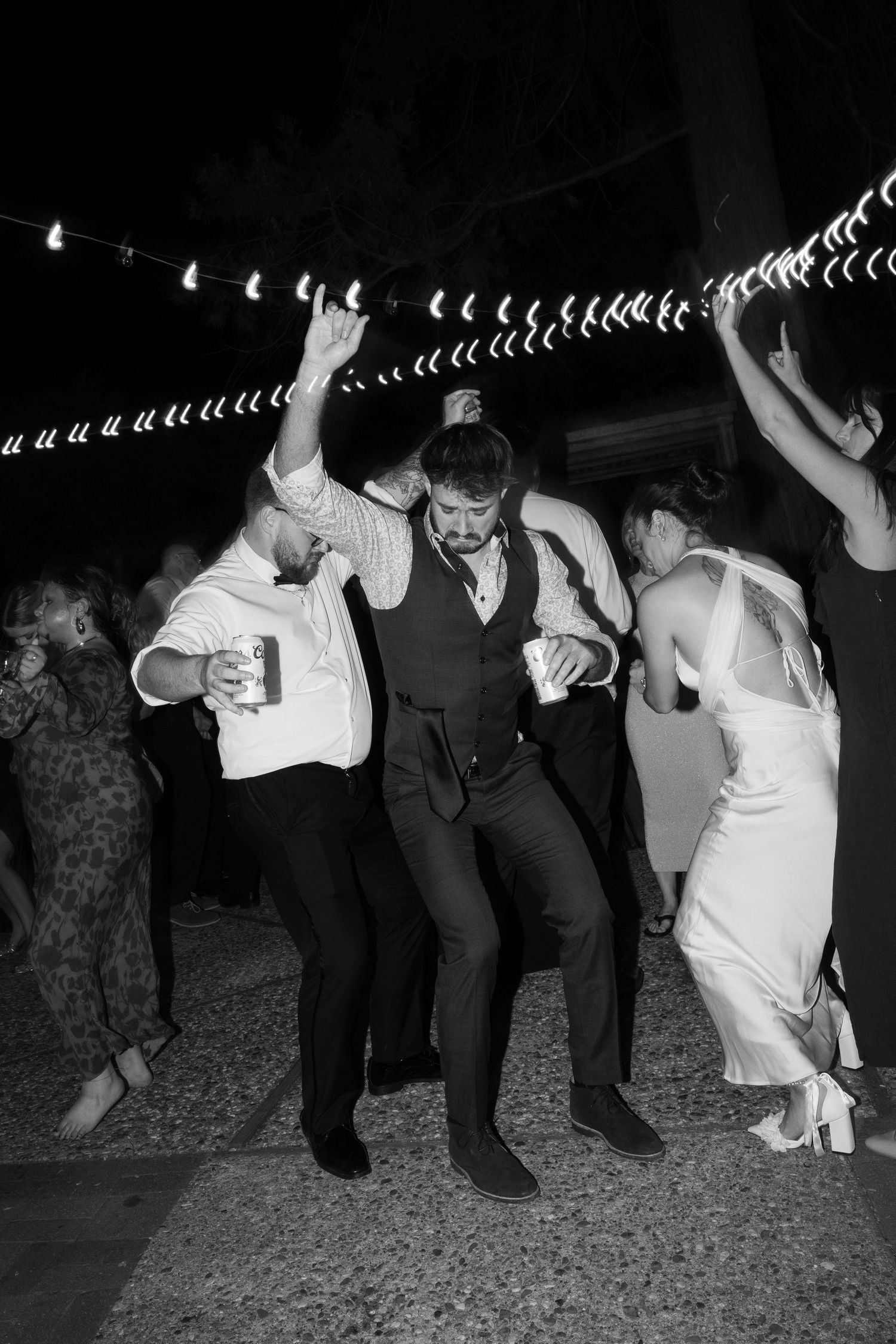 Black and white photo of wedding guests dancing in a line formation at a reception celebration.