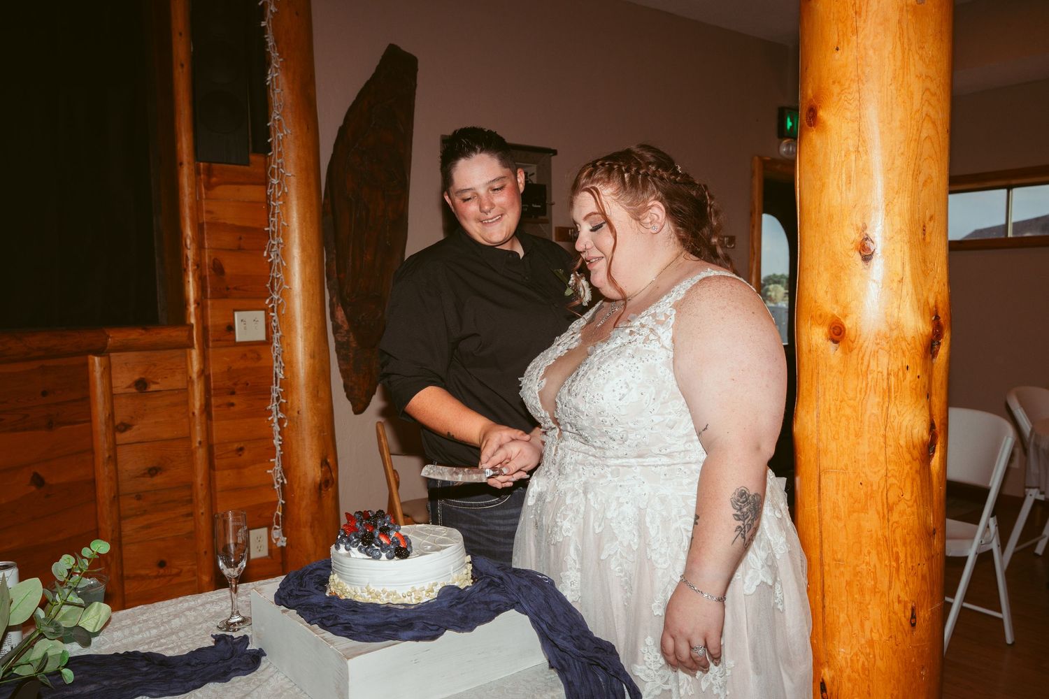 Newlyweds prepare to cut their wedding cake inside a rustic wooden venue.
