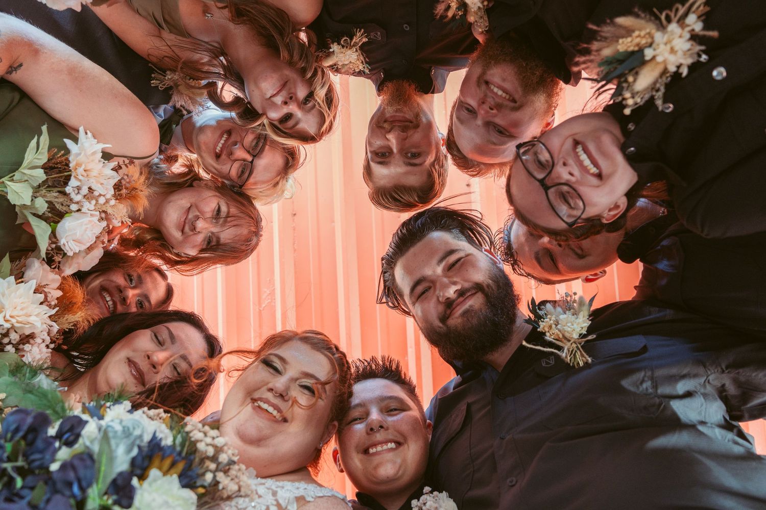 Circle of people looking down at camera creating fun wedding photo composition.